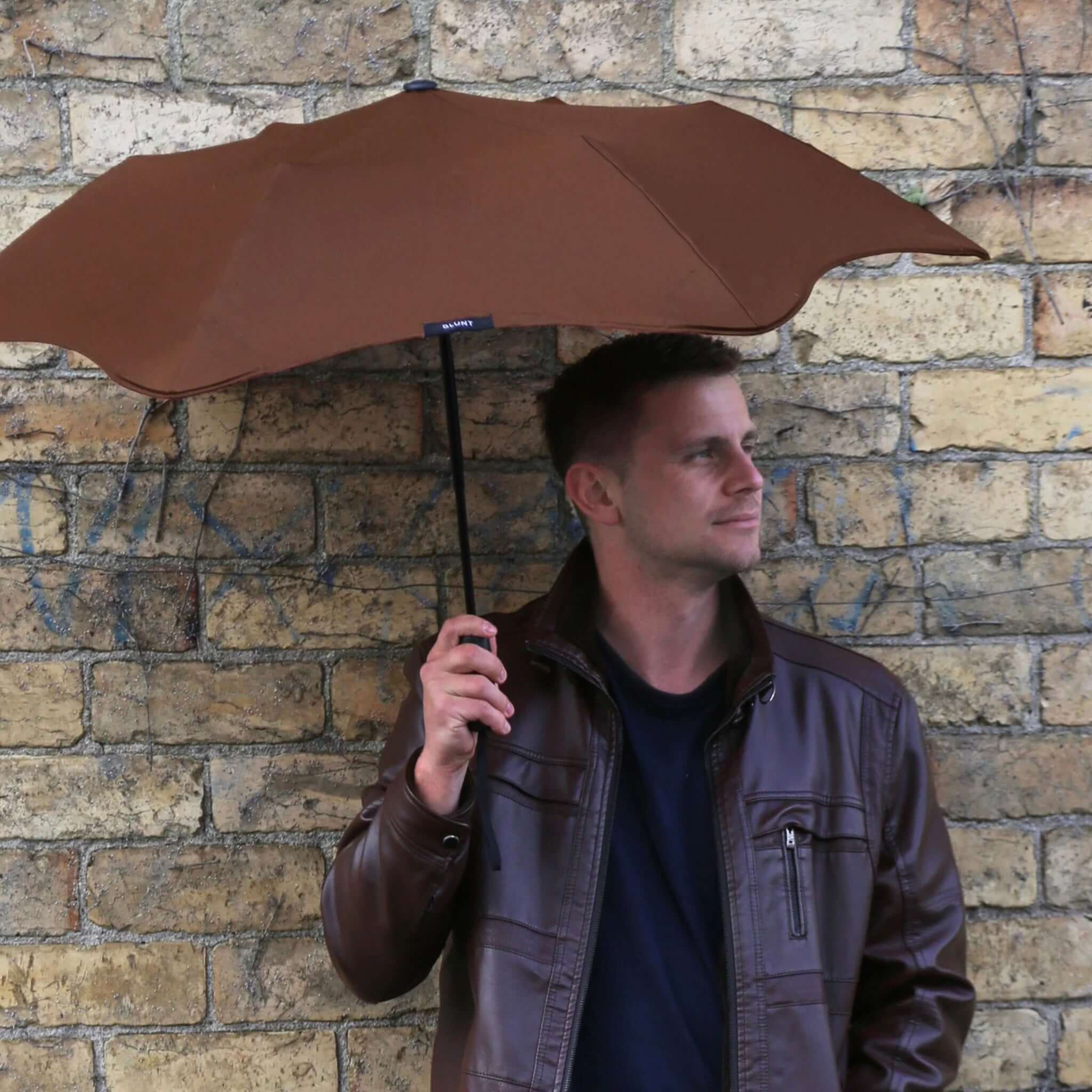 Alt Tag: Blunt Metro Core Range Umbrella open canopy held by man against brick wall, compact urban umbrella with 100cm coverage
