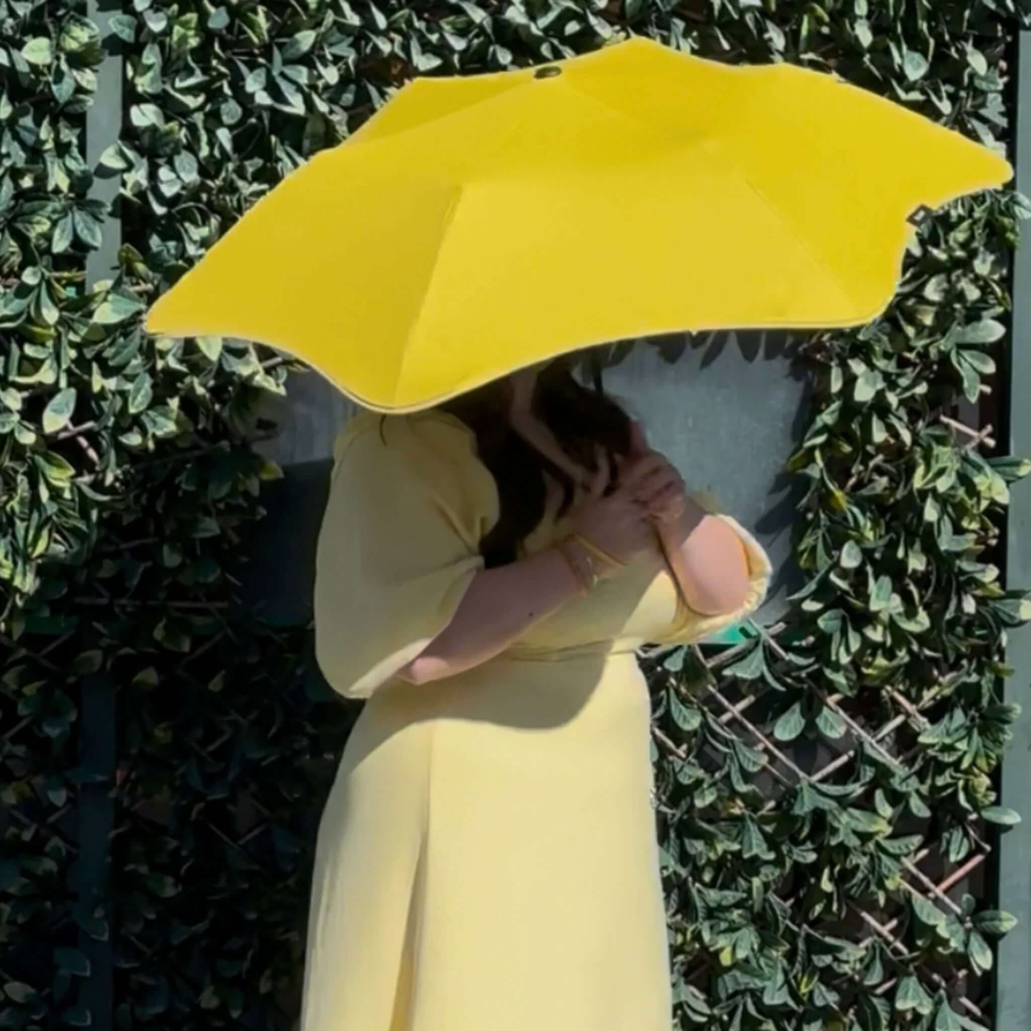 Person holding a yellow umbrella against a green leafy background