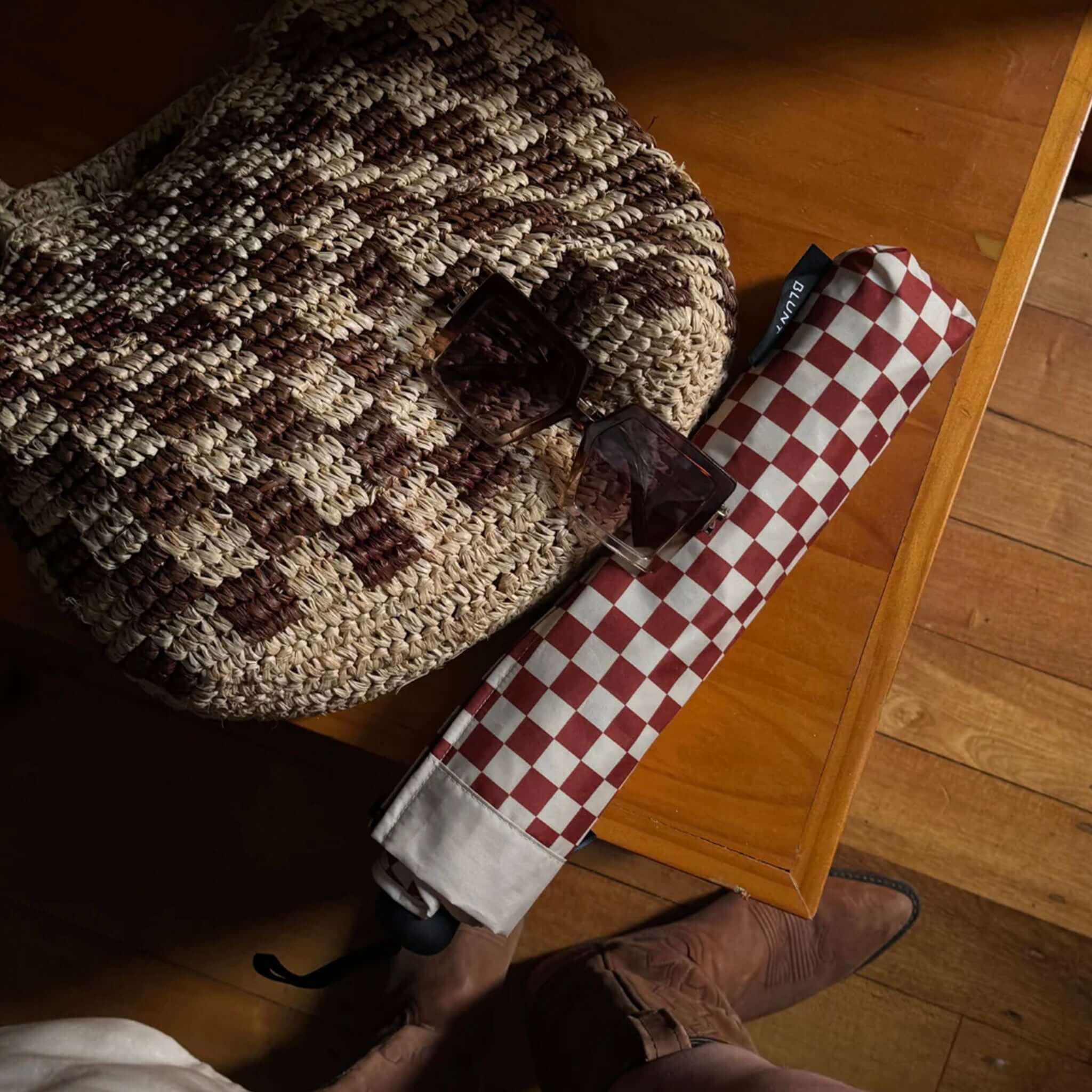 Blunt Metro Umbrella - Clay Check Limited Edition placed beside a woven bag and sunglasses on a wooden table.
