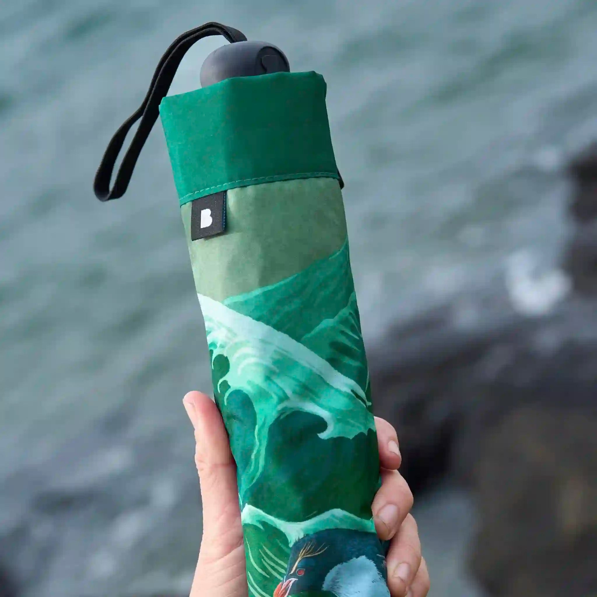 Green umbrella with wave design held by a hand against a water background