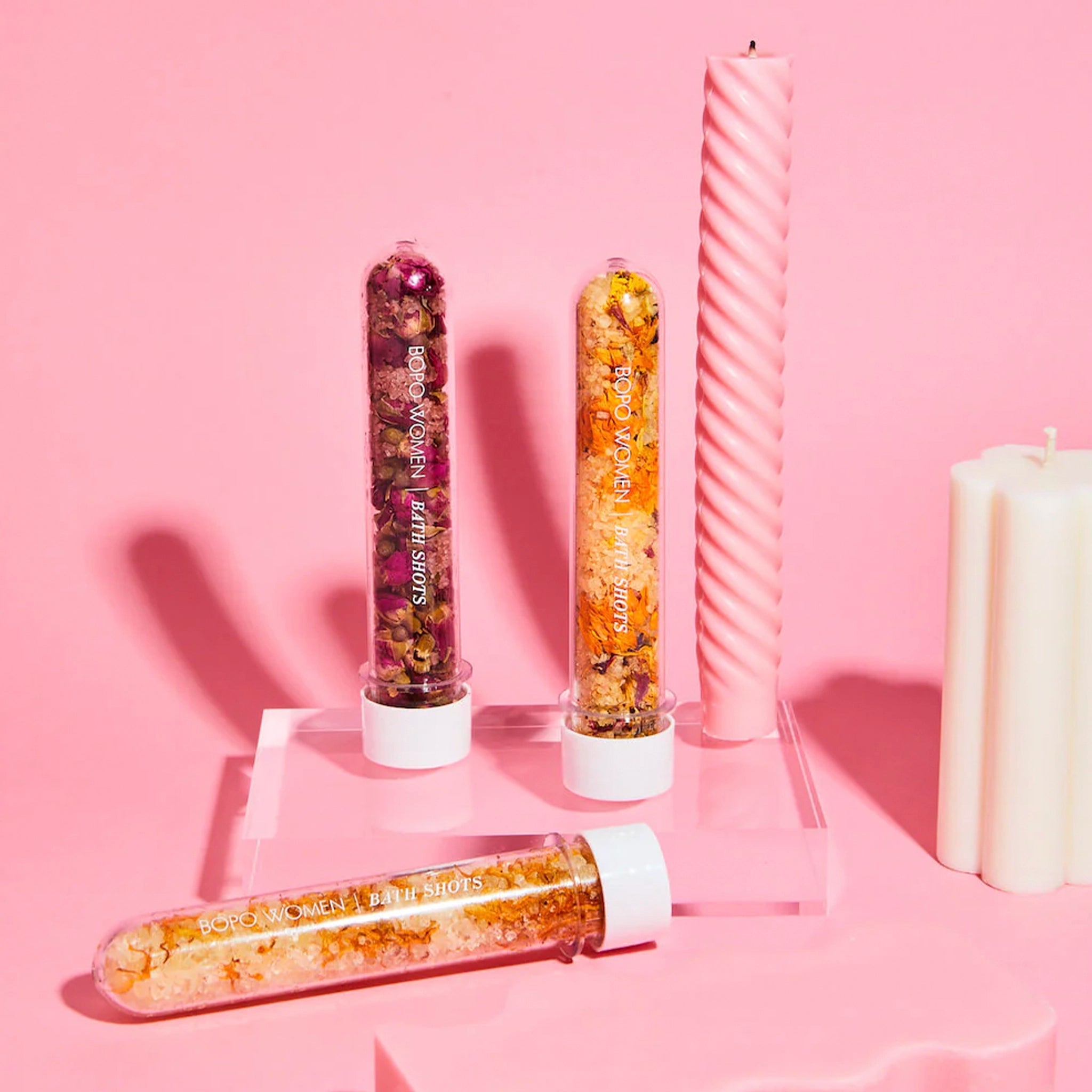 Three decorative vials with colorful contents on a pink background