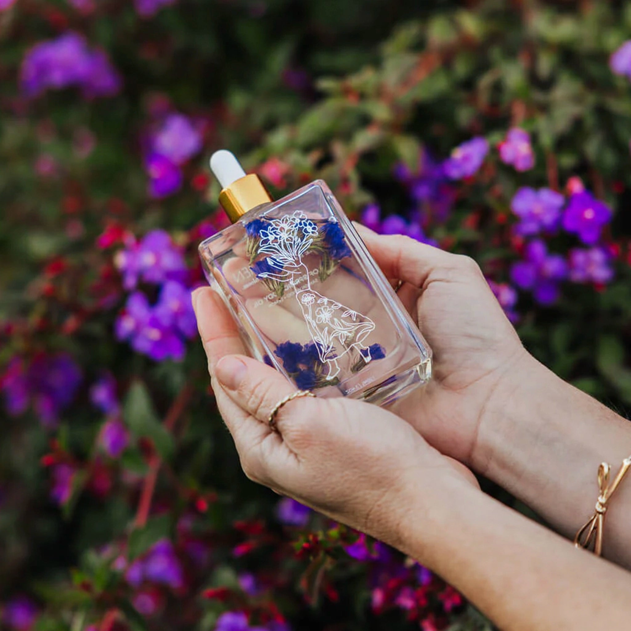Woman holding a bottle of body oil with floral design and gold cap 