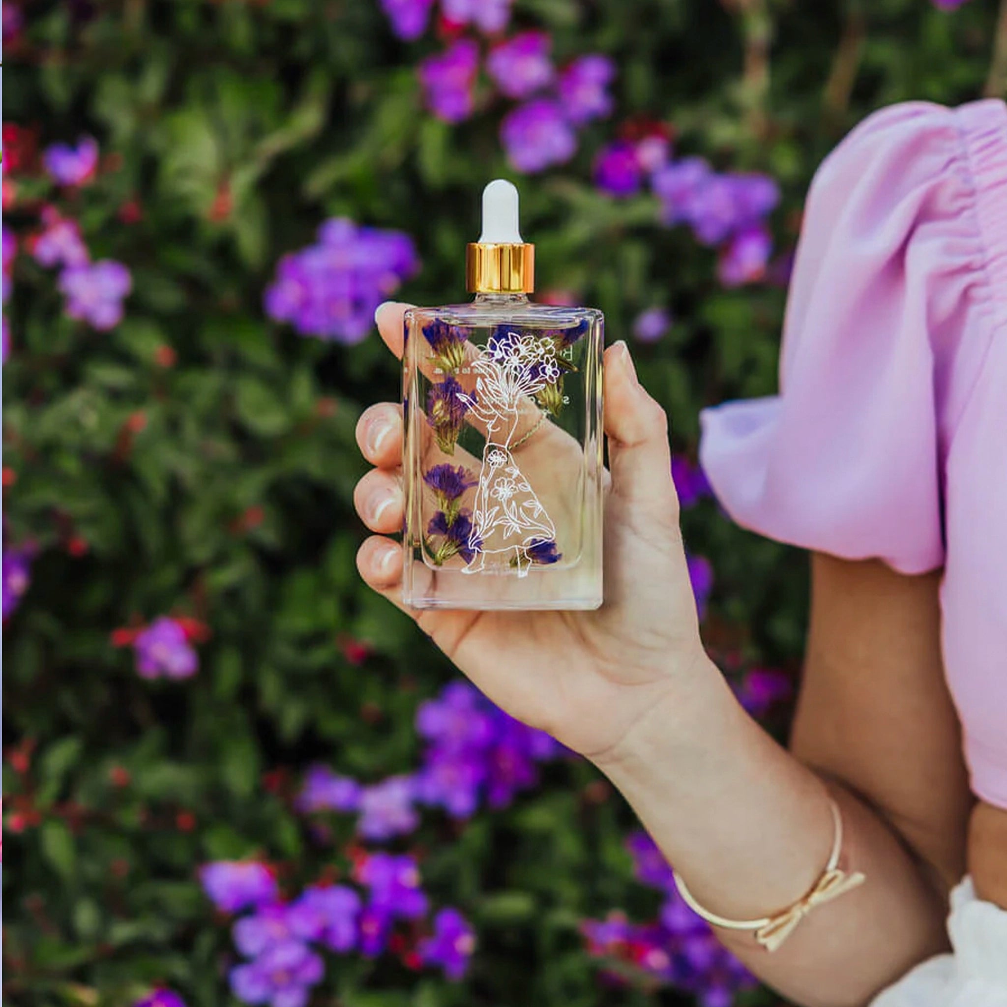 Woman holding a bottle of body oil with floral design and gold cap 