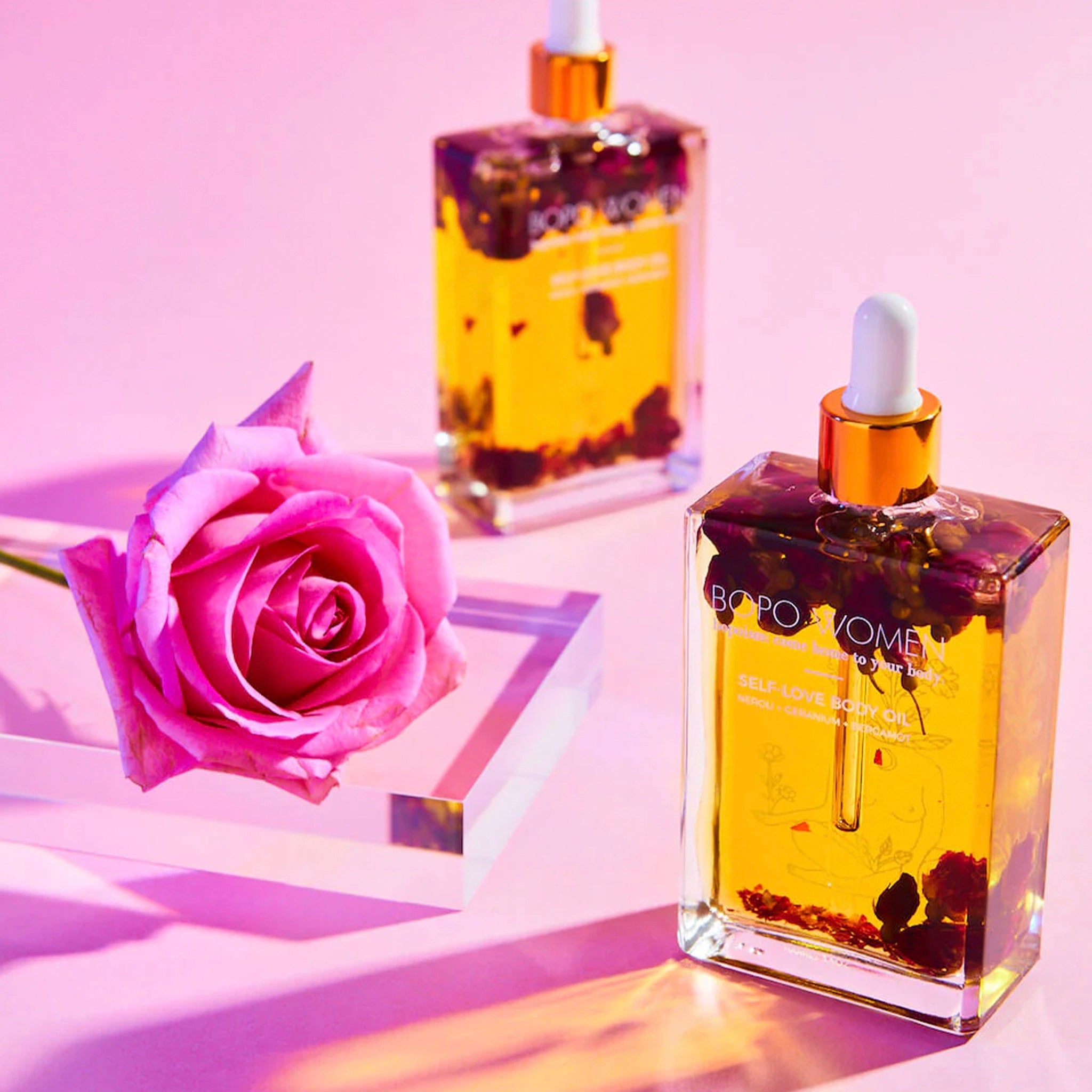 Bottle of Bopo Women self-love body oil with dried flowers on a pink background