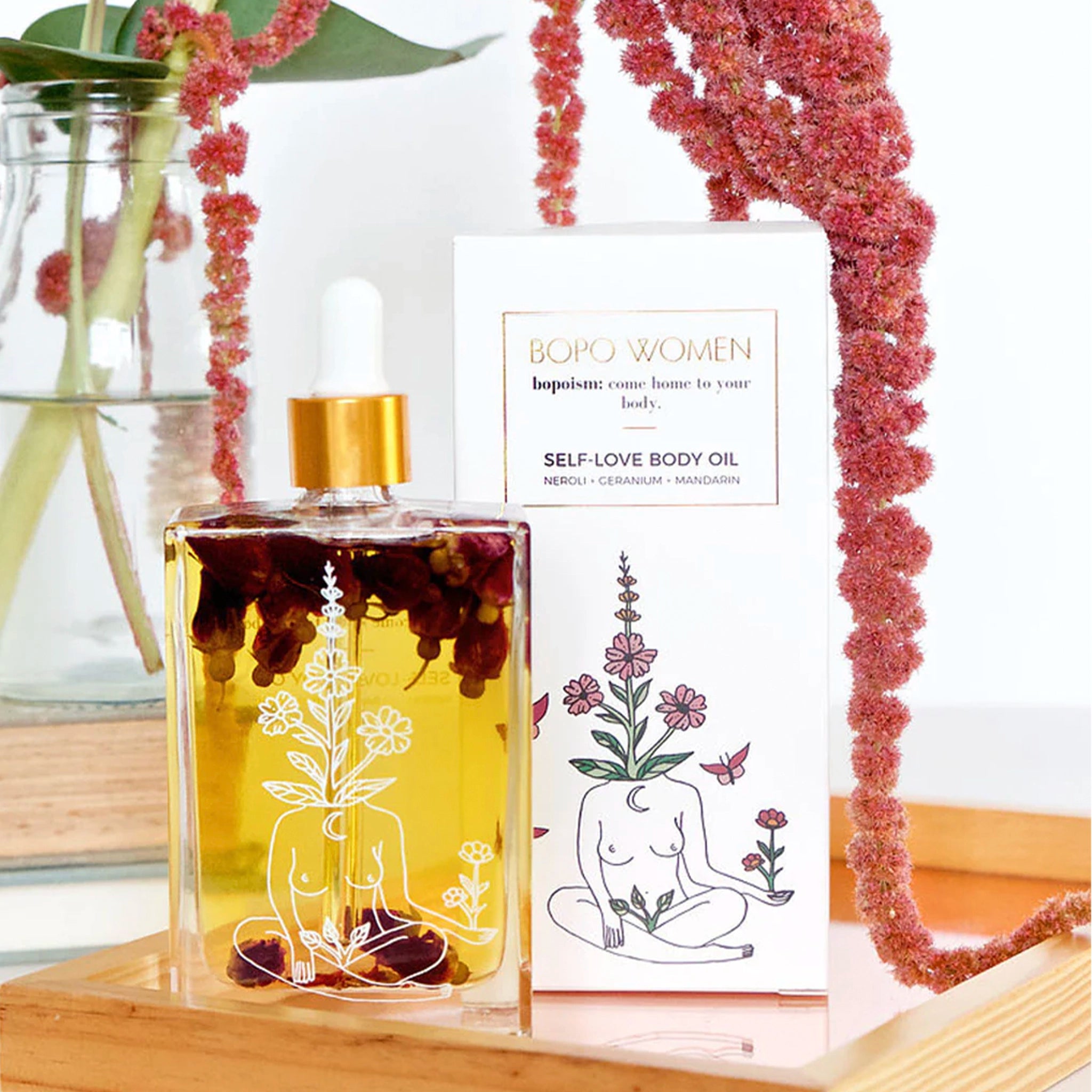 Bottle of Bopo Women self-love body oil with dried flowers on a white background
