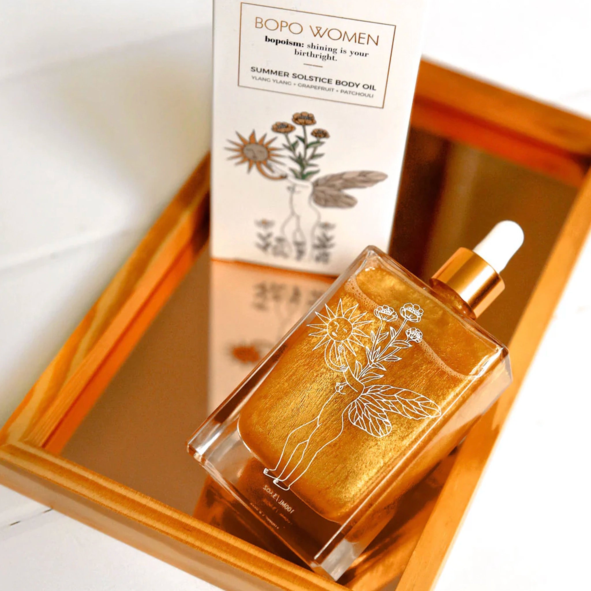 Gold bottle of BOPO Women body oil with packaging on a reflective surface