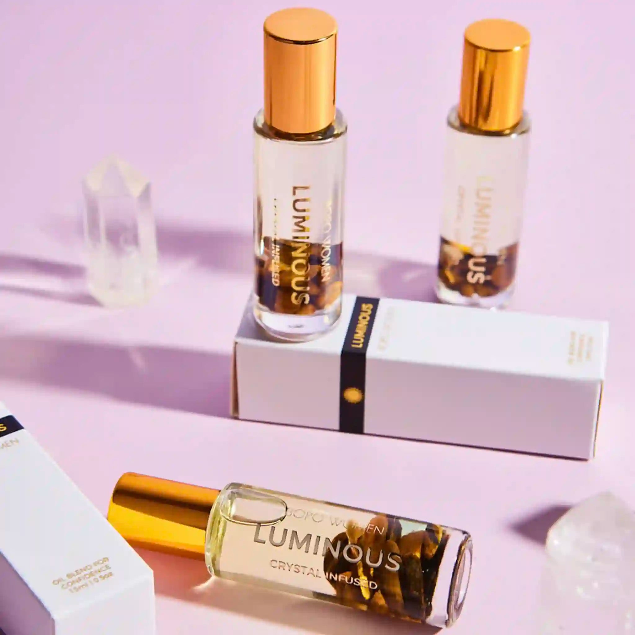 Three bottles of Luminous perfume with gold caps on a light purple background