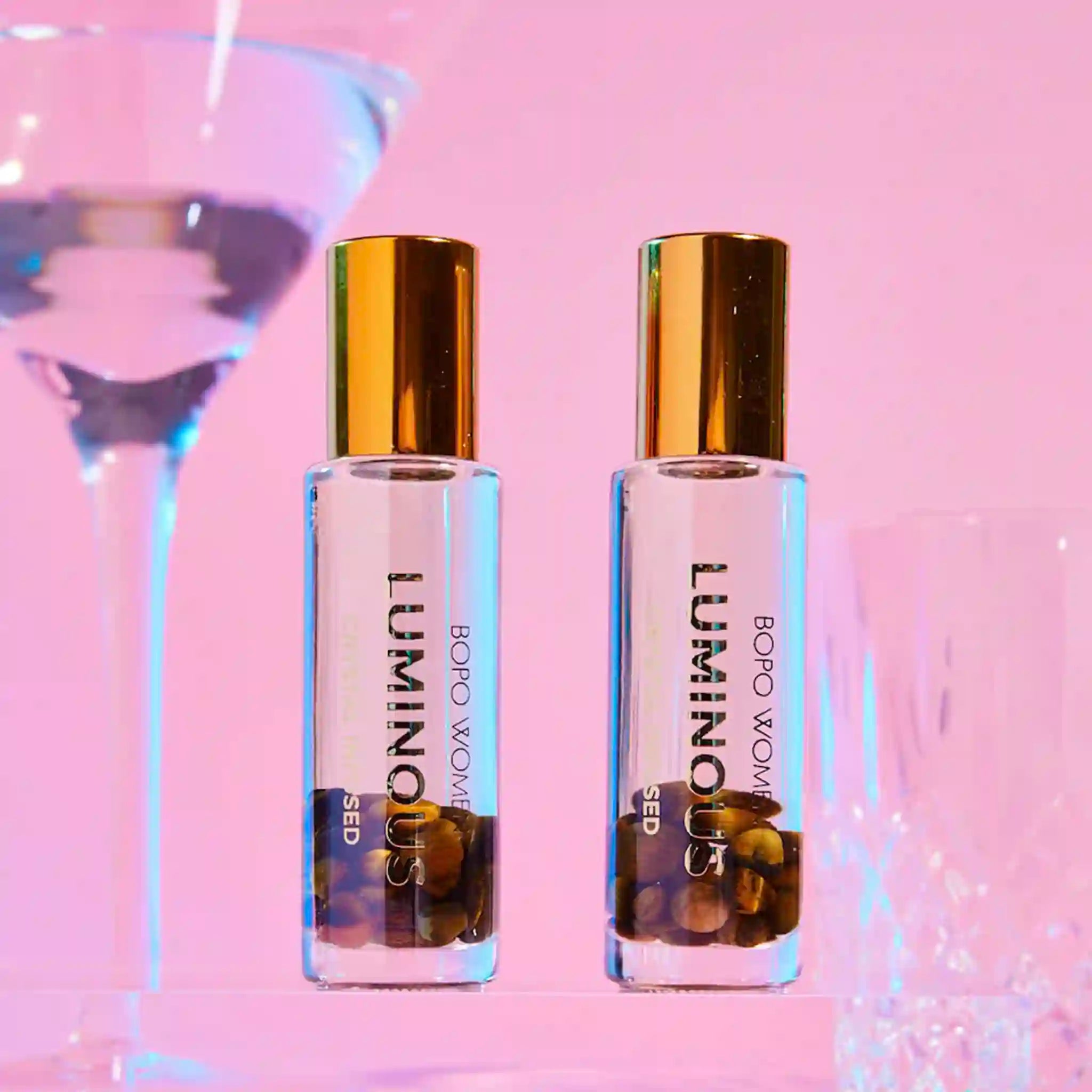Two bottles of Luminous perfume with gold caps on a light purple background