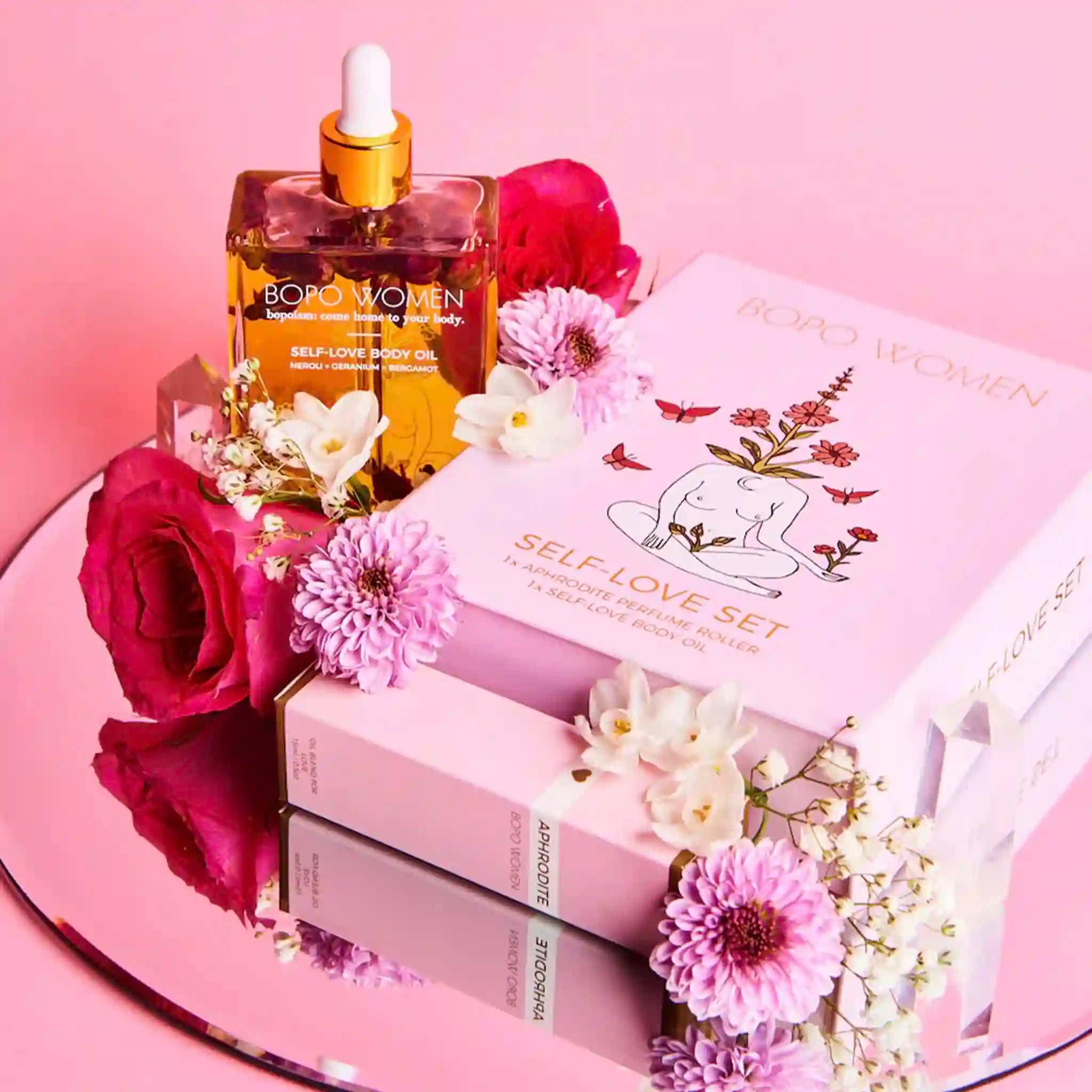 BOBO WOMEN self-love body oil bottle and packaging with flowers on a pink background