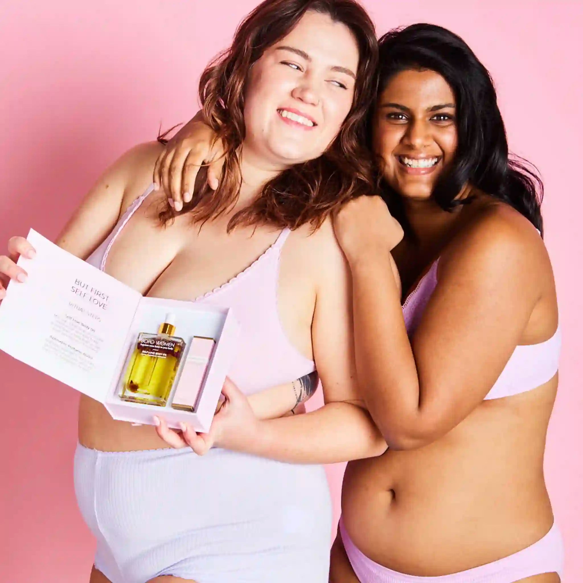 Two women in pink lingerie holding a magazine with a product on a pink background