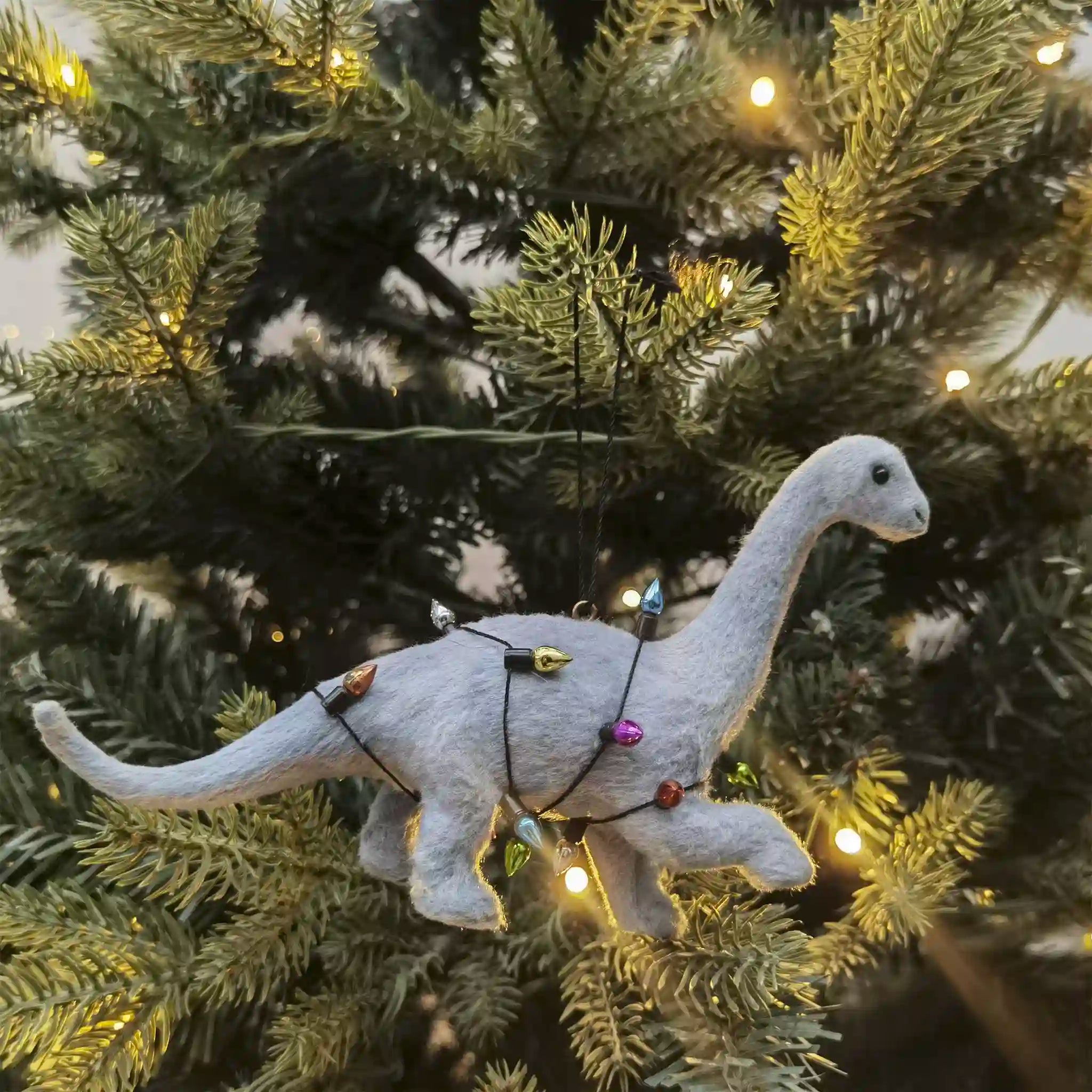 Dinosaur ornament on a decorated Christmas tree with lights.