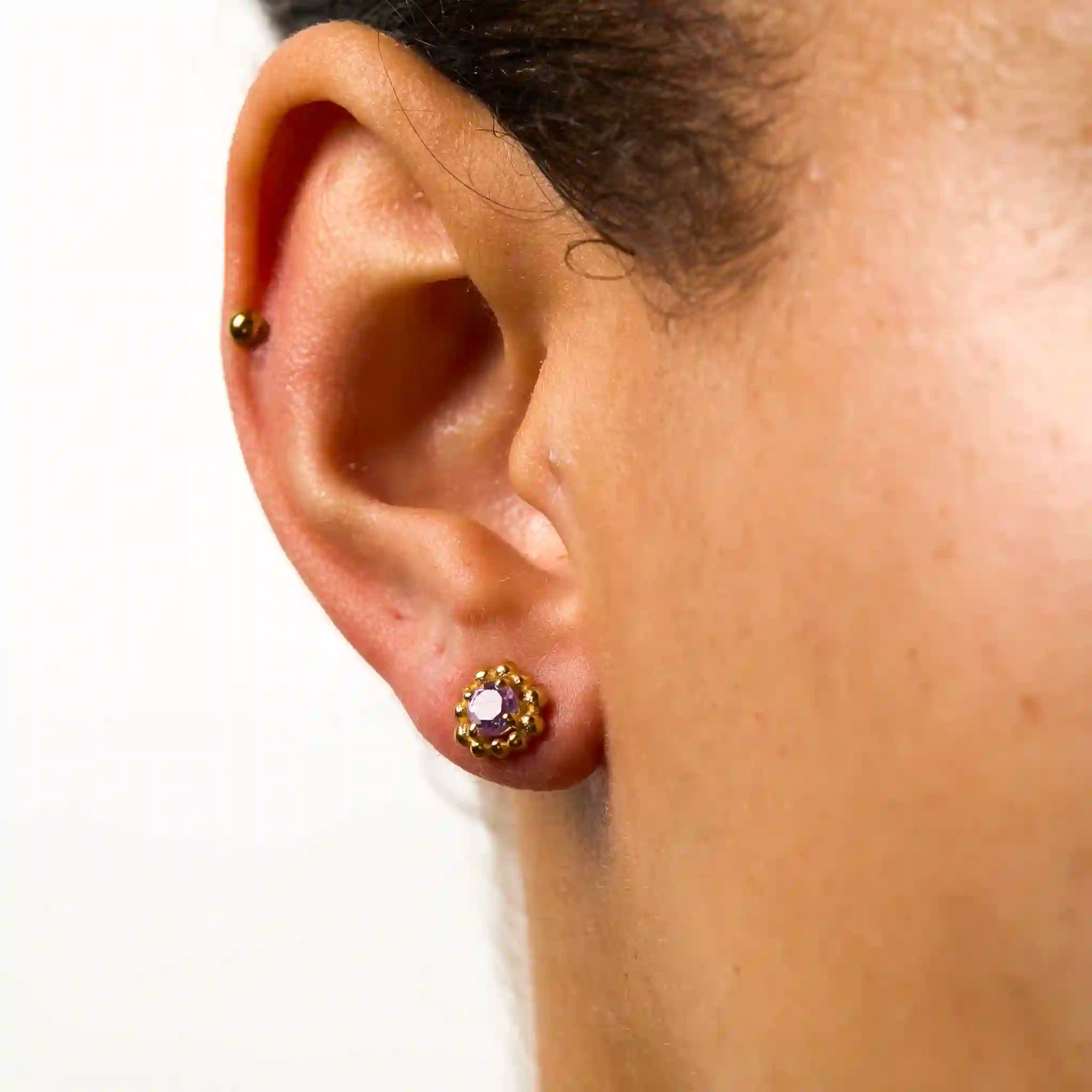 Close-up of an ear wearing a gold earring with a clear gemstone on a white background