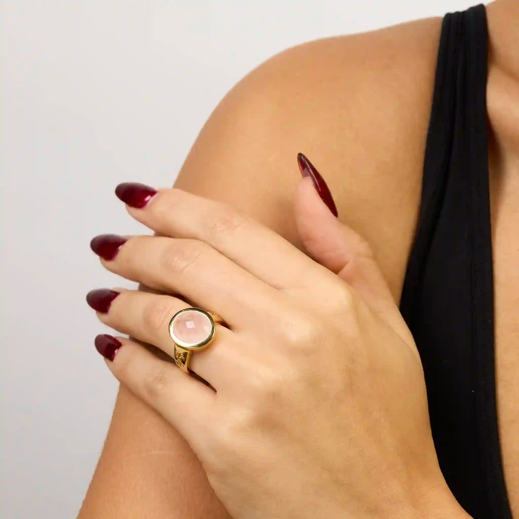 Hand wearing a ring with a pink stone, against a neutral background