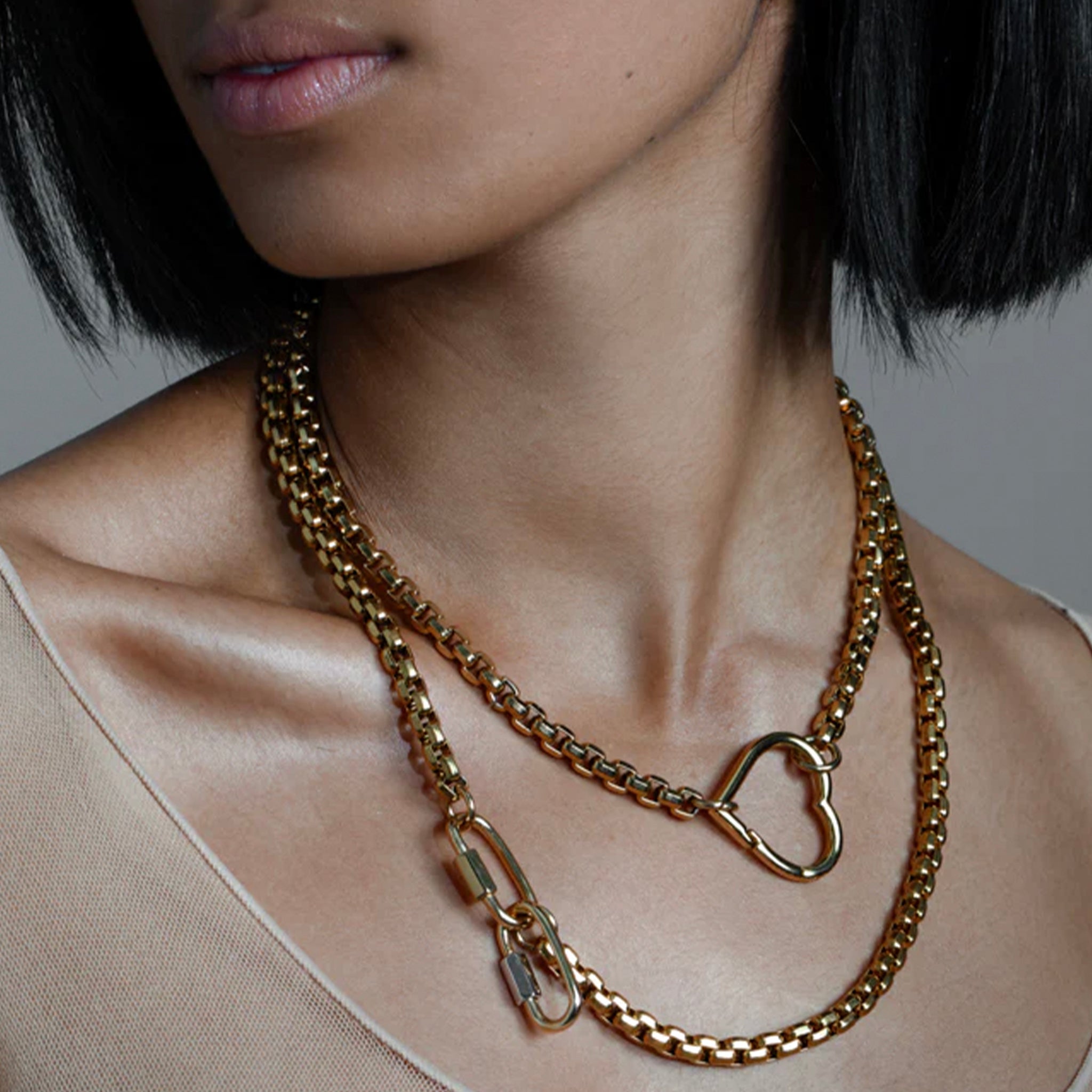 Close-up of a person wearing a gold chain necklace with a heart-shaped clasp.