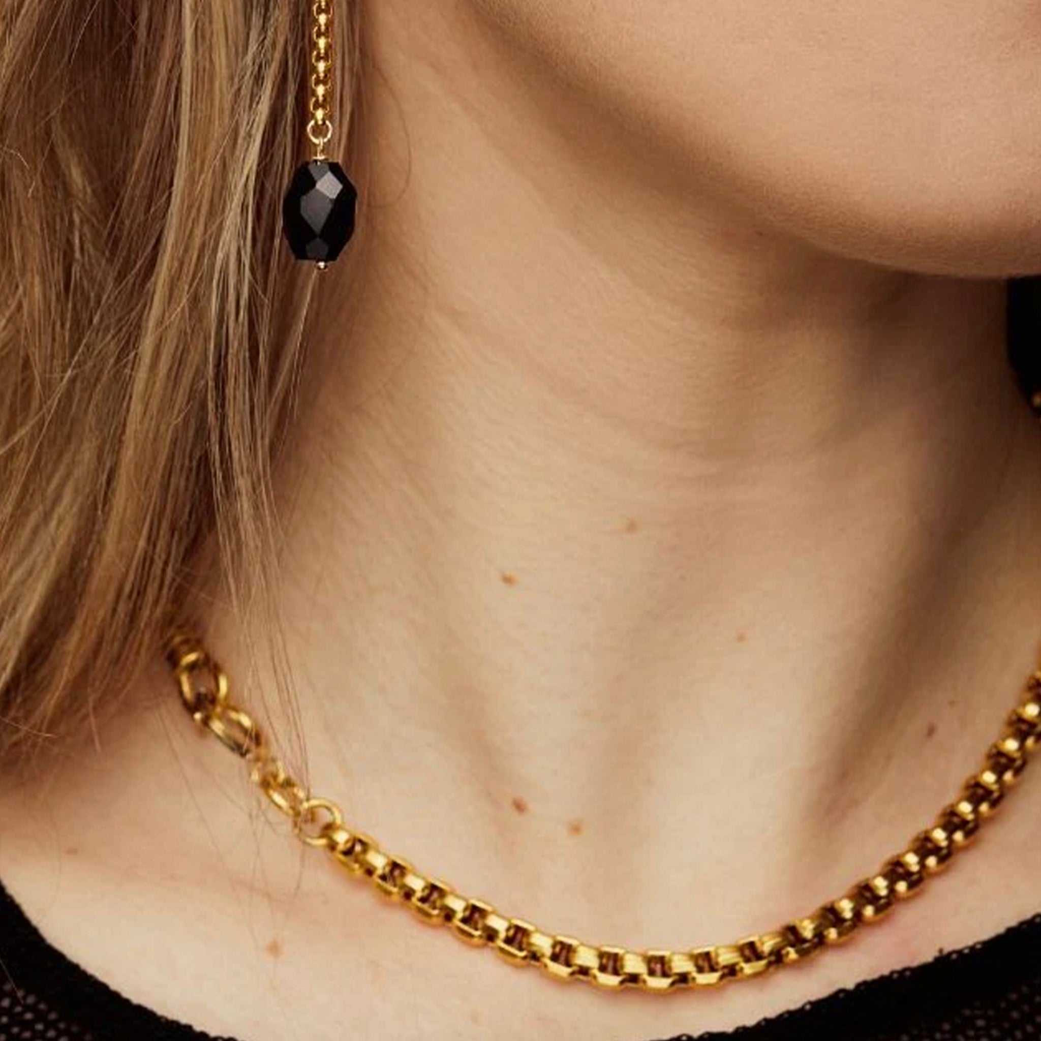 Close-up of a person wearing a gold chain necklace and black earring.