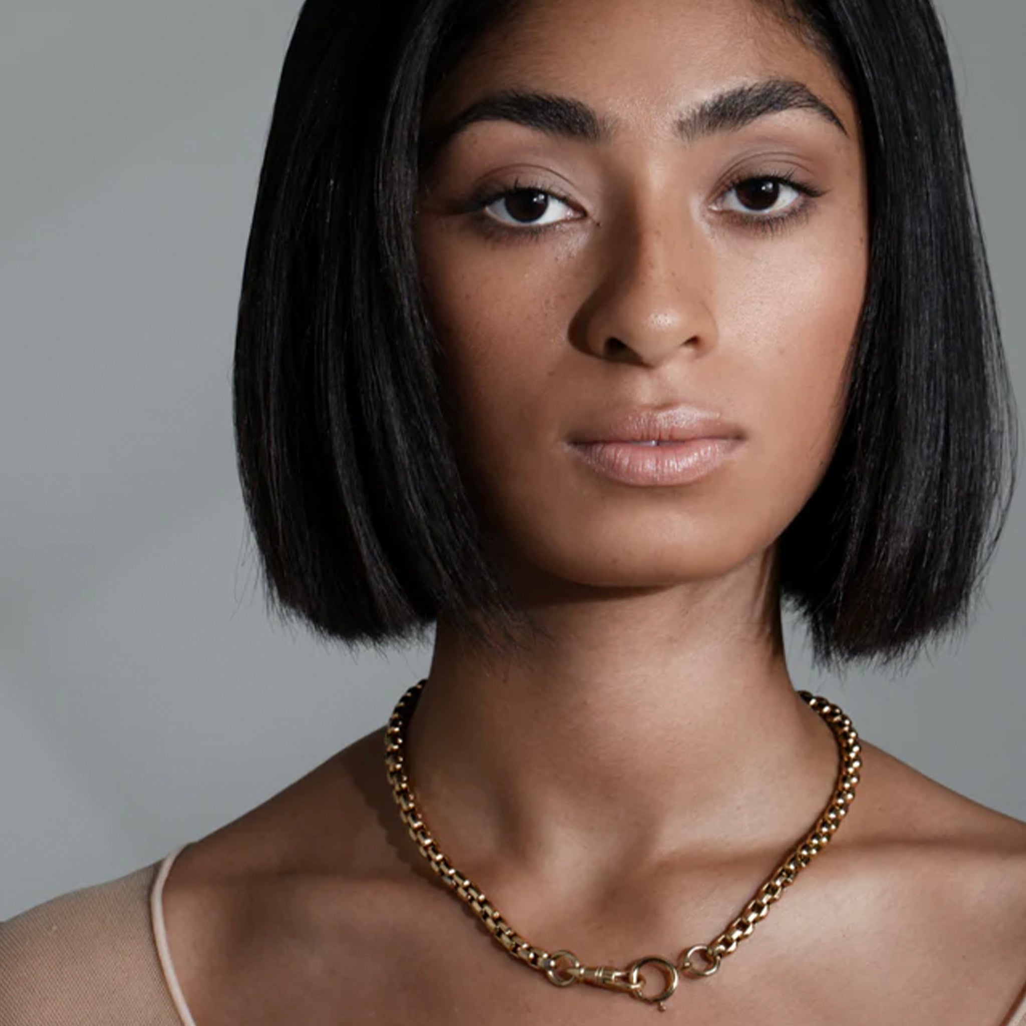 Woman wearing a gold chain necklace against a gray background