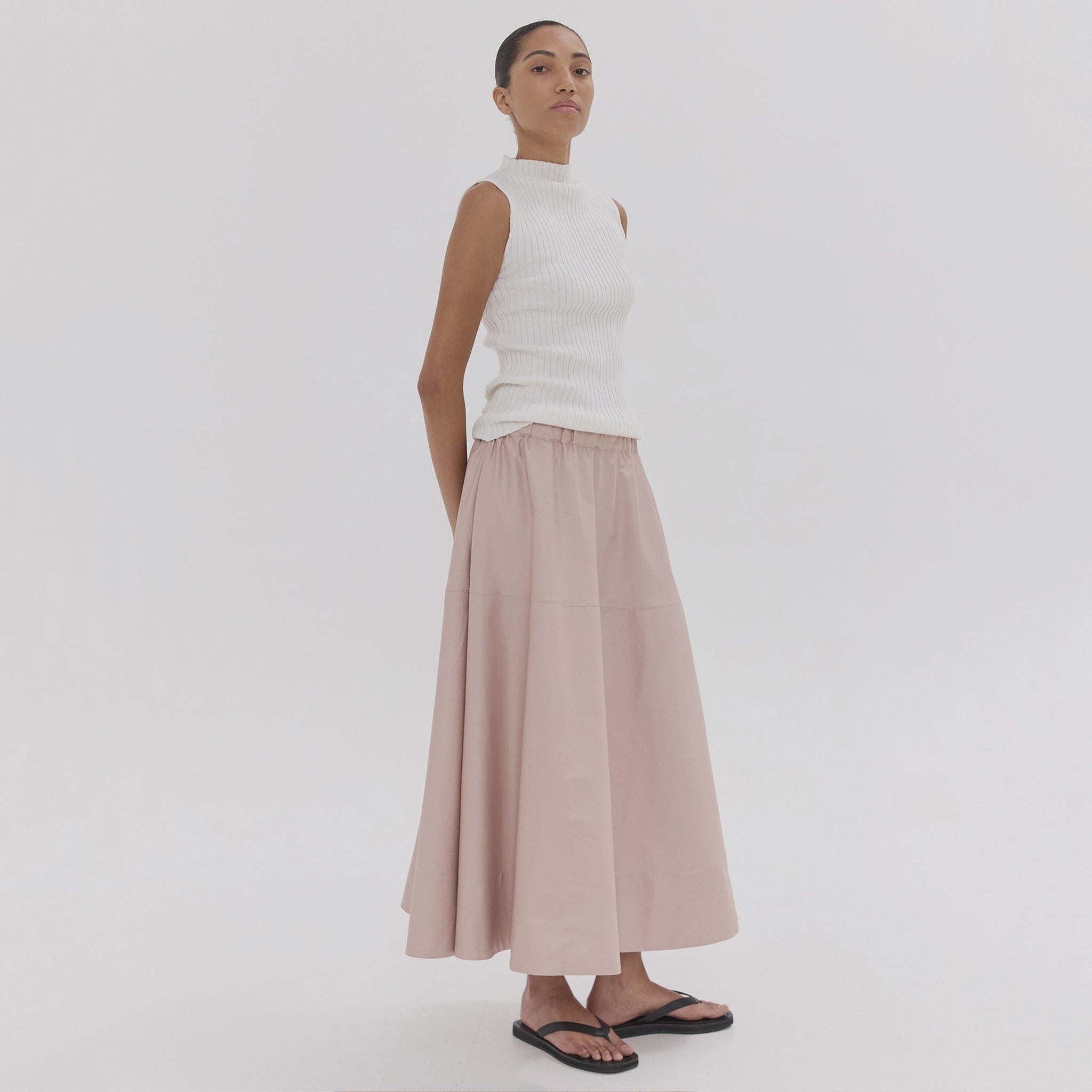 Woman wearing a white sleeveless top and pink skirt on a white background
