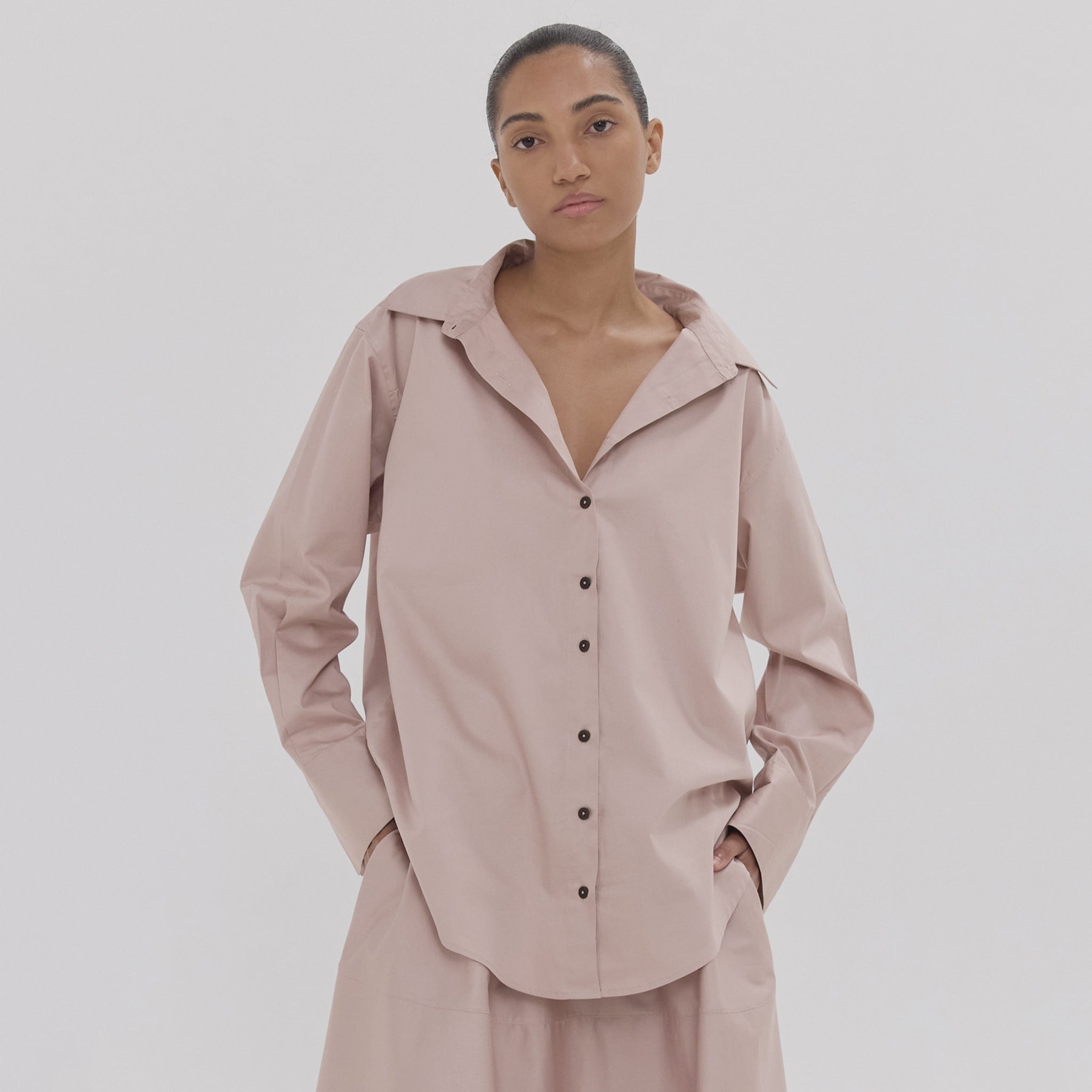 Person wearing a light pink outfit with black buttons on a white background