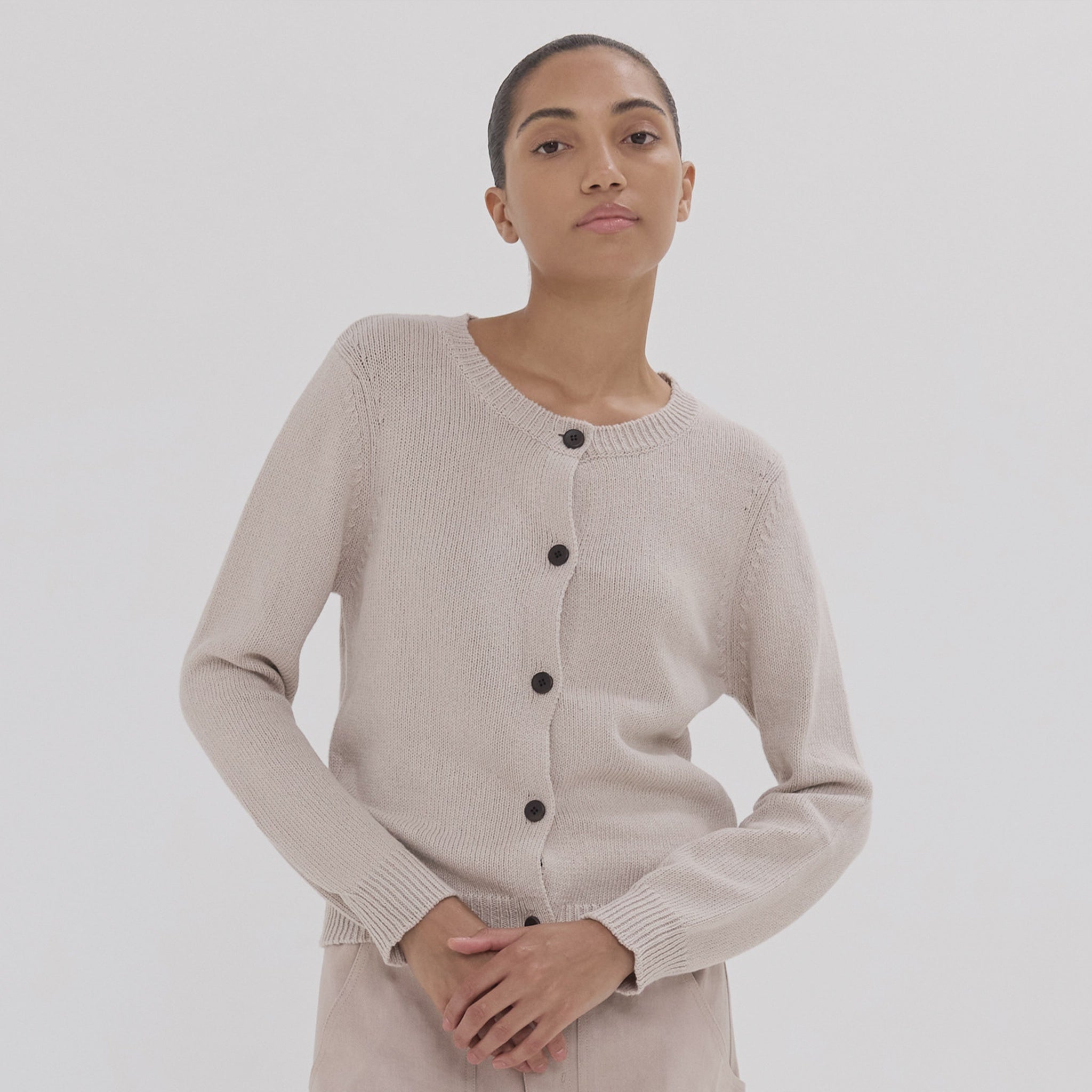 Woman wearing a beige cardigan with black buttons on a white background