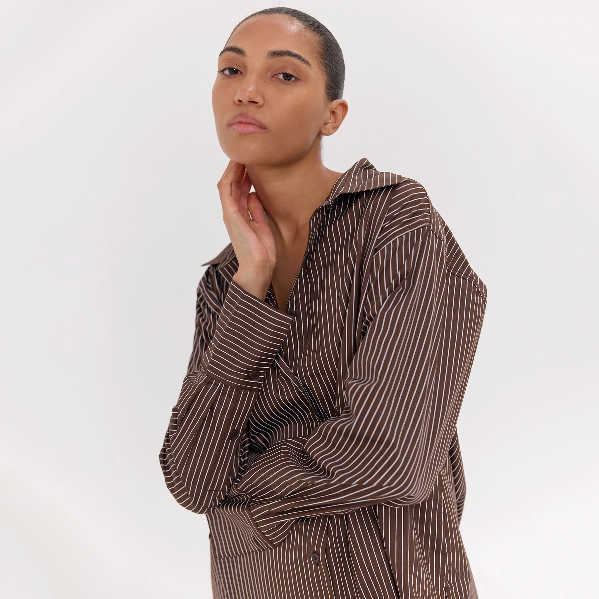 Woman wearing a brown and white striped shirt against a white background