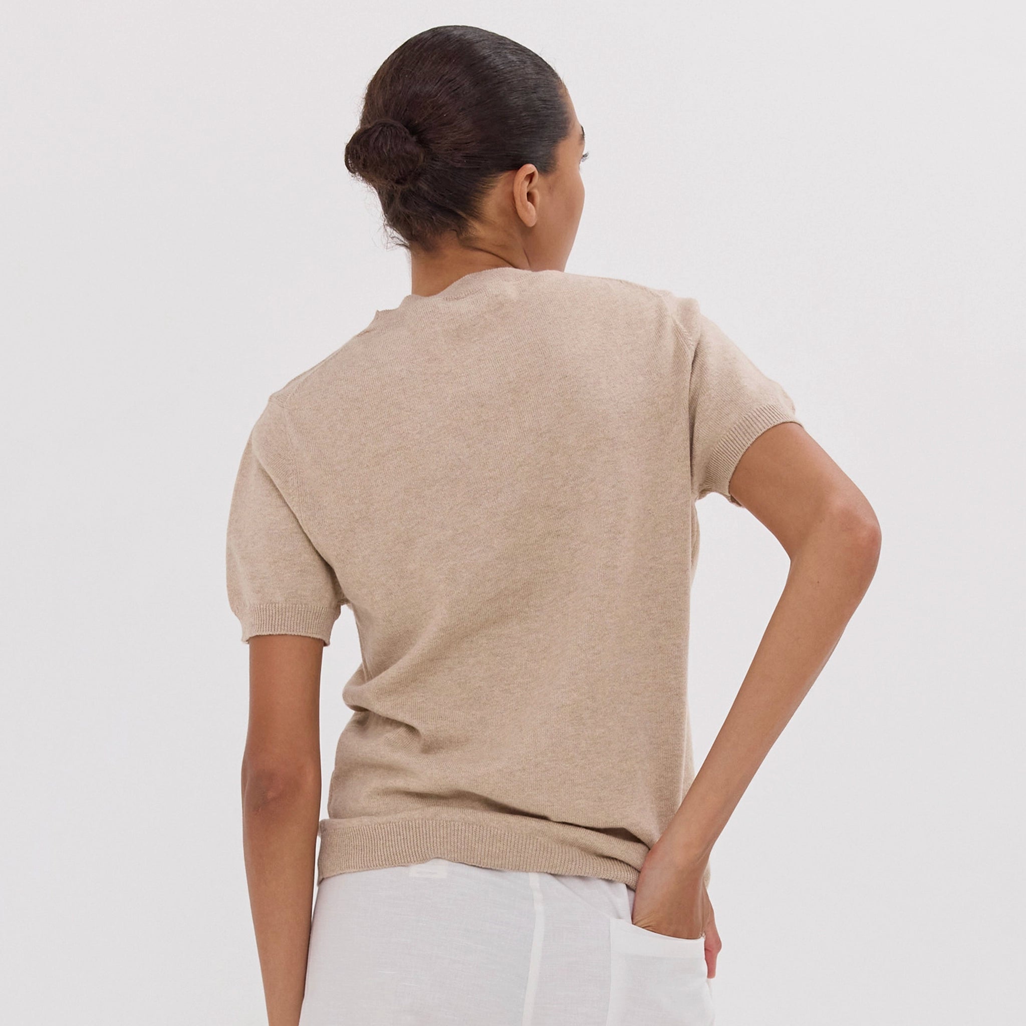 Woman wearing a beige sweater and white pants against a plain background