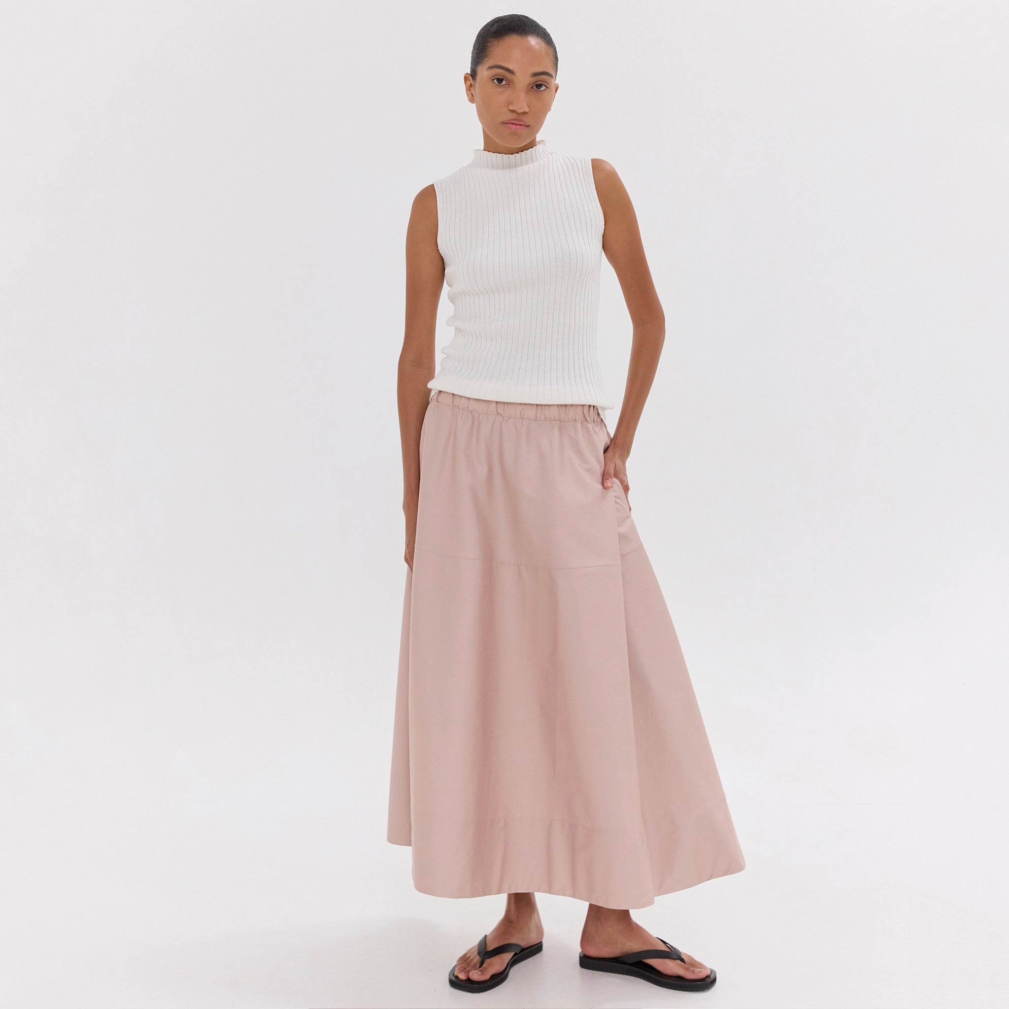Woman wearing a white sleeveless top and pink skirt on a white background