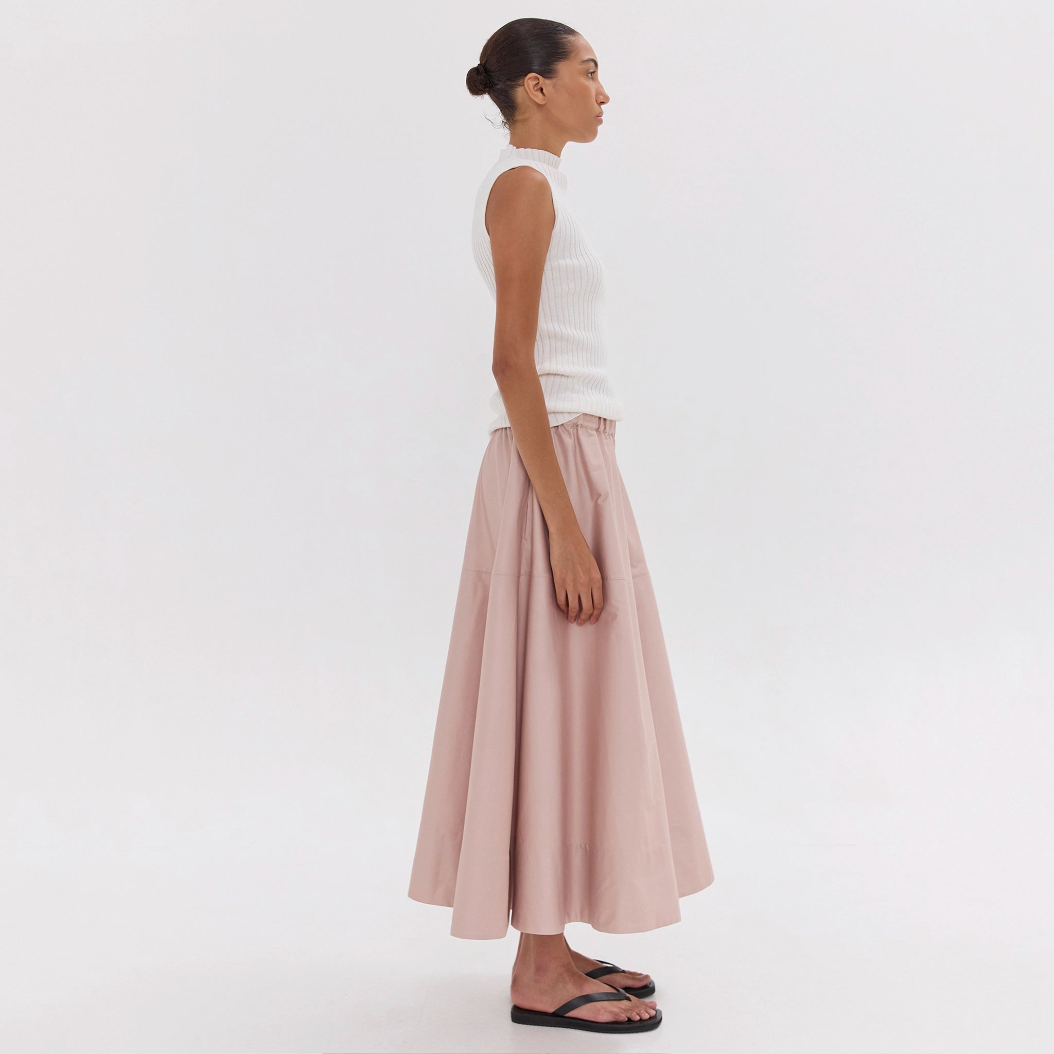 Woman wearing a white sleeveless top and pink skirt on a white background