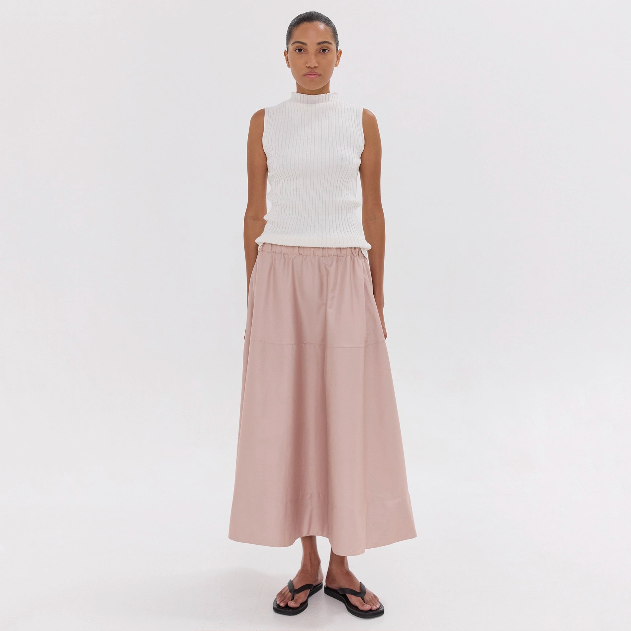 Woman wearing a white sleeveless top and beige skirt on a white background
