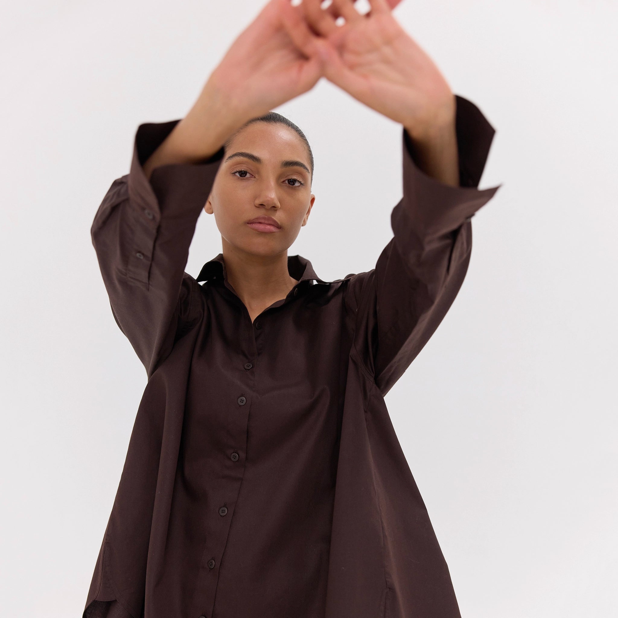 Person wearing a brown shirt with arms raised against a white background