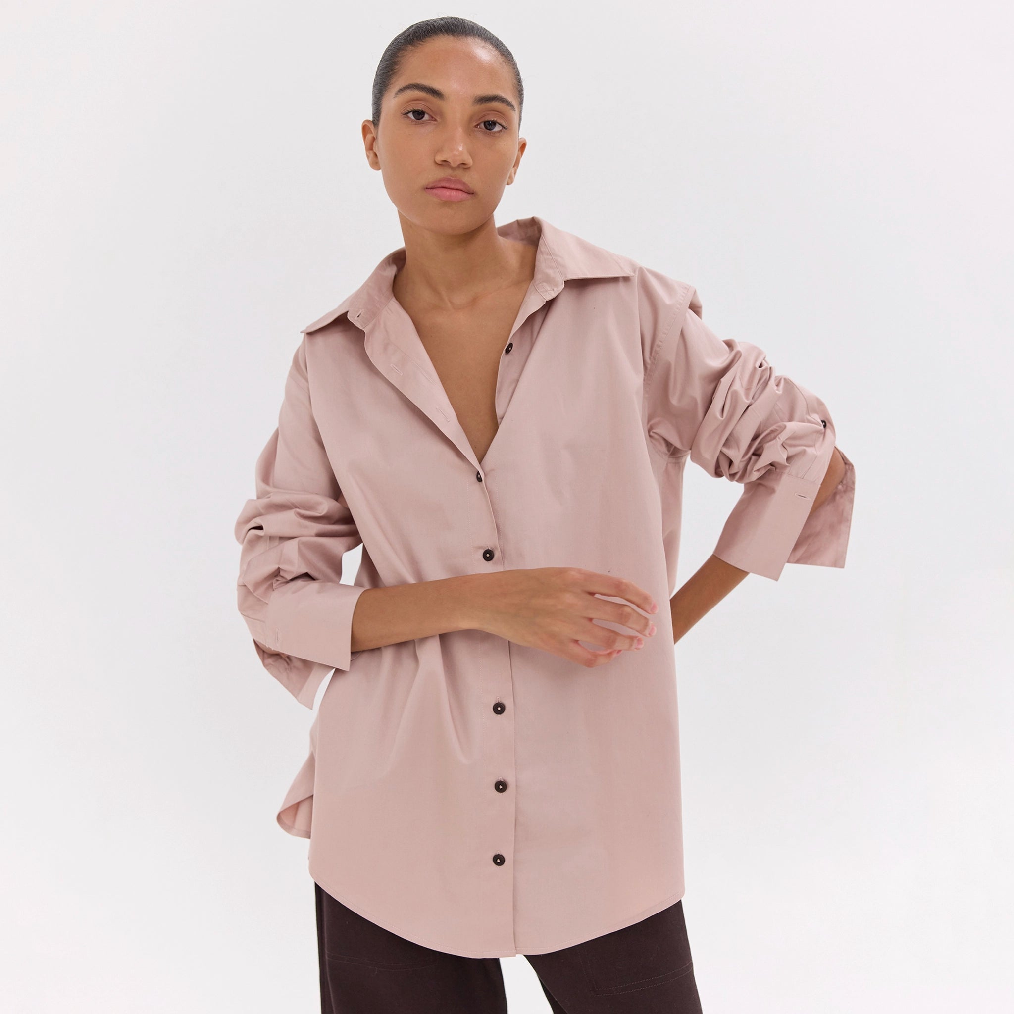 Woman wearing a light pink shirt with black buttons on a white background