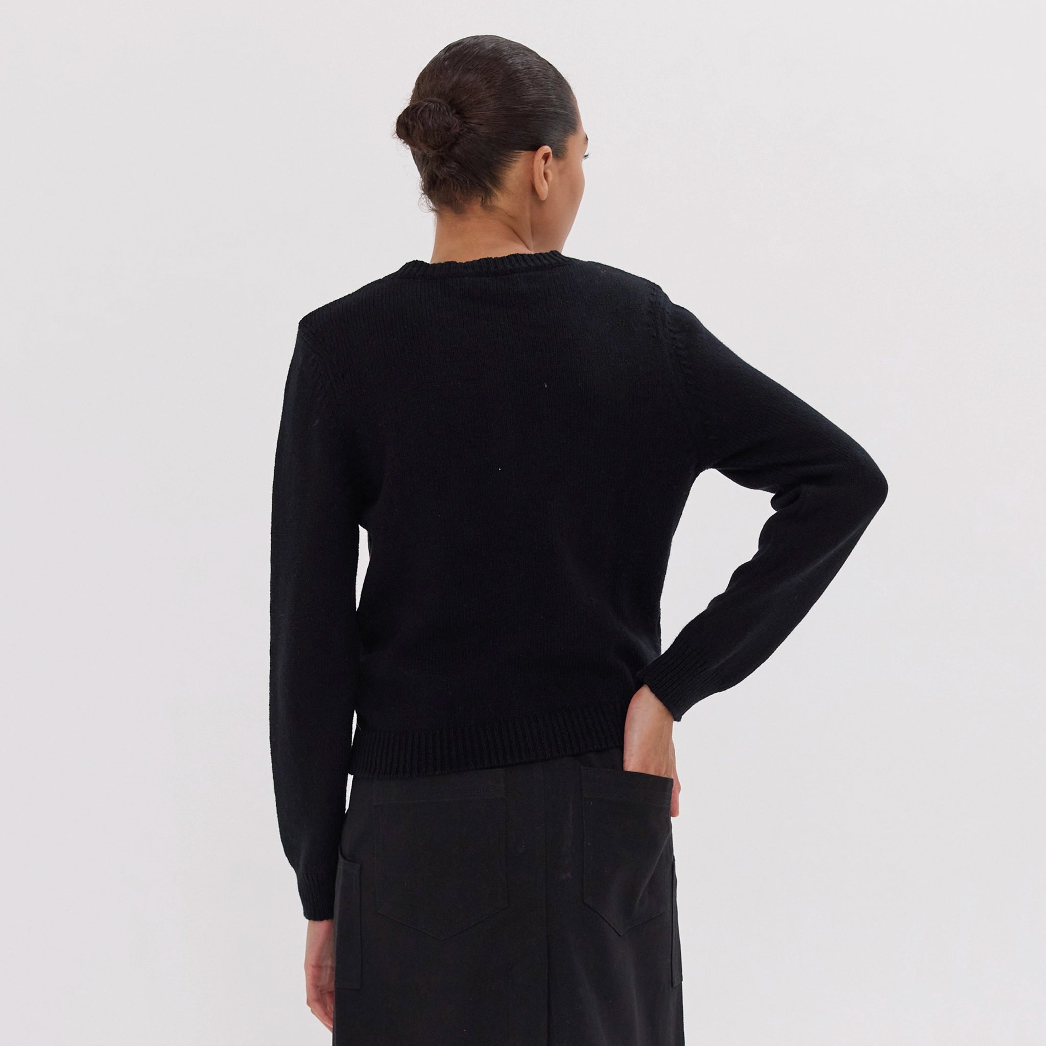 Person wearing a black sweater and dark pants on a light gray background