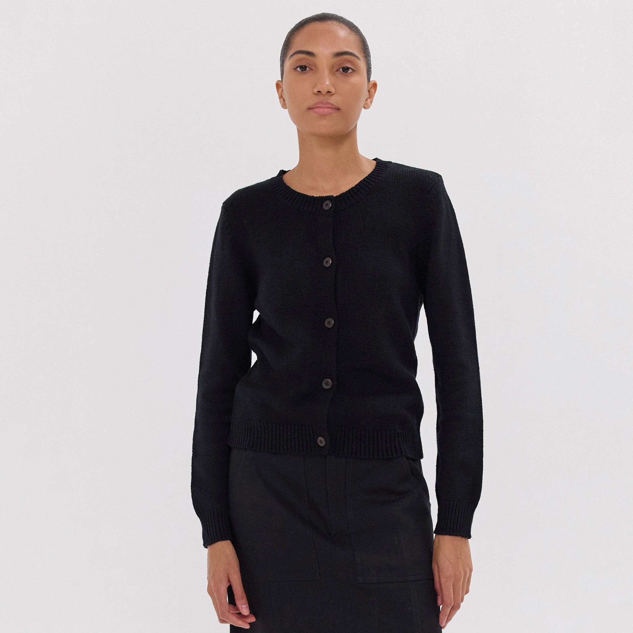 Woman wearing a black cardigan and skirt set against a white background