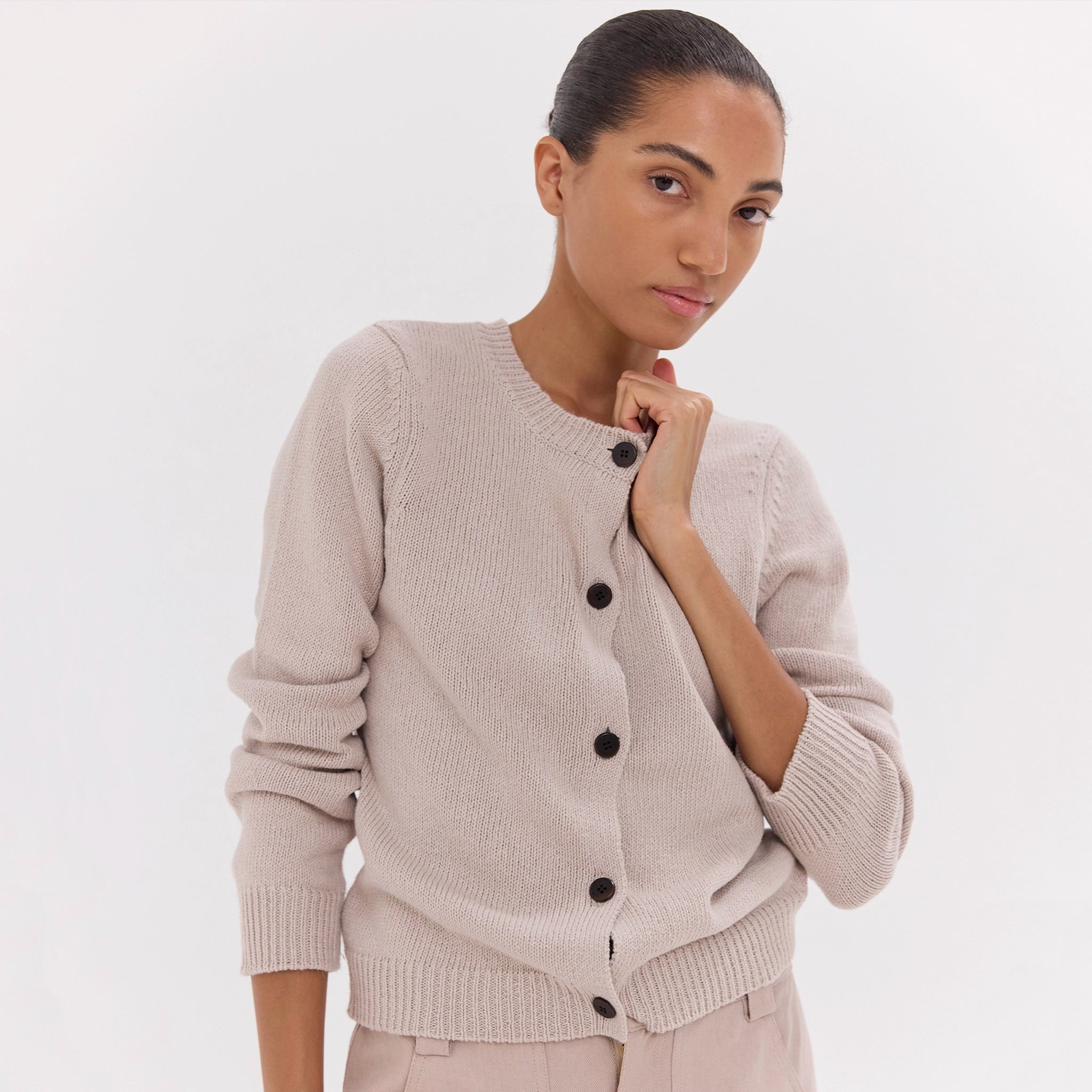 Woman wearing a beige cardigan with black buttons on a white background