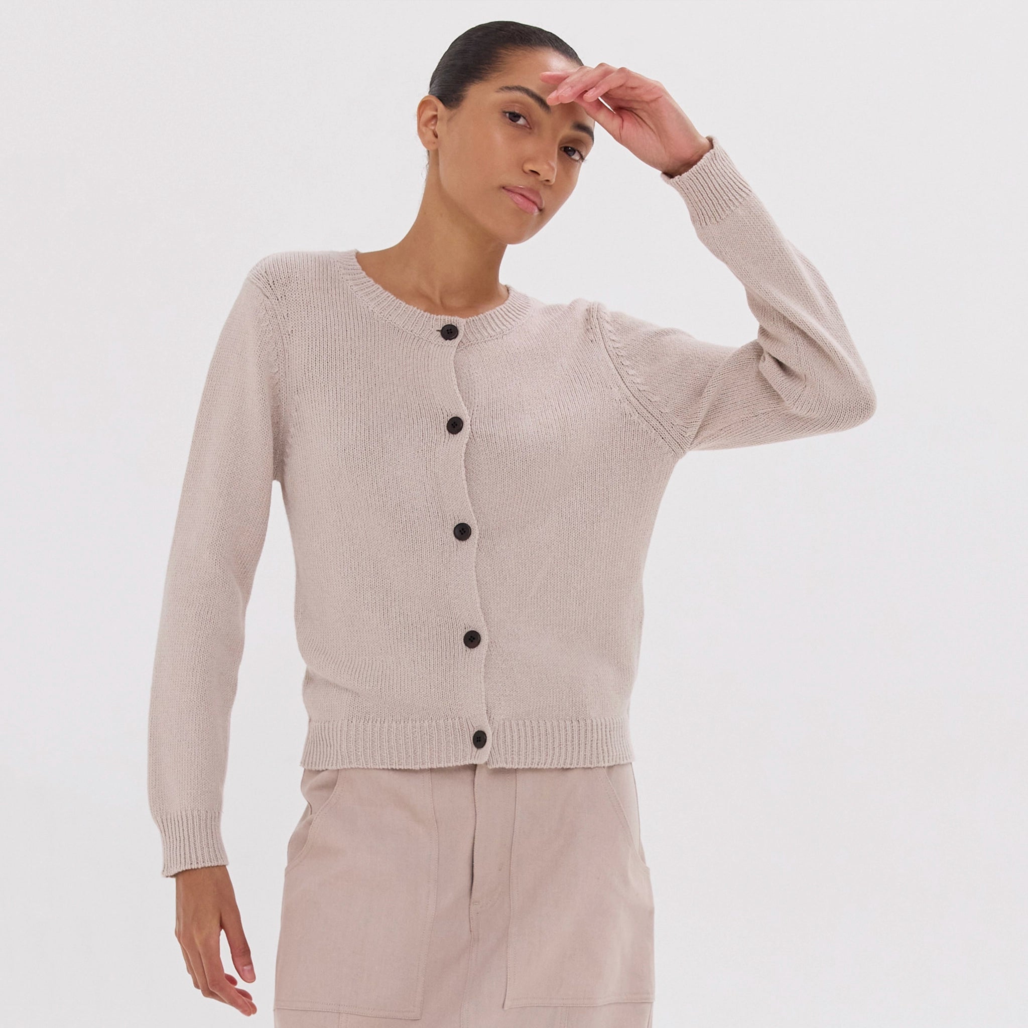 Woman wearing a beige cardigan with black buttons on a white background