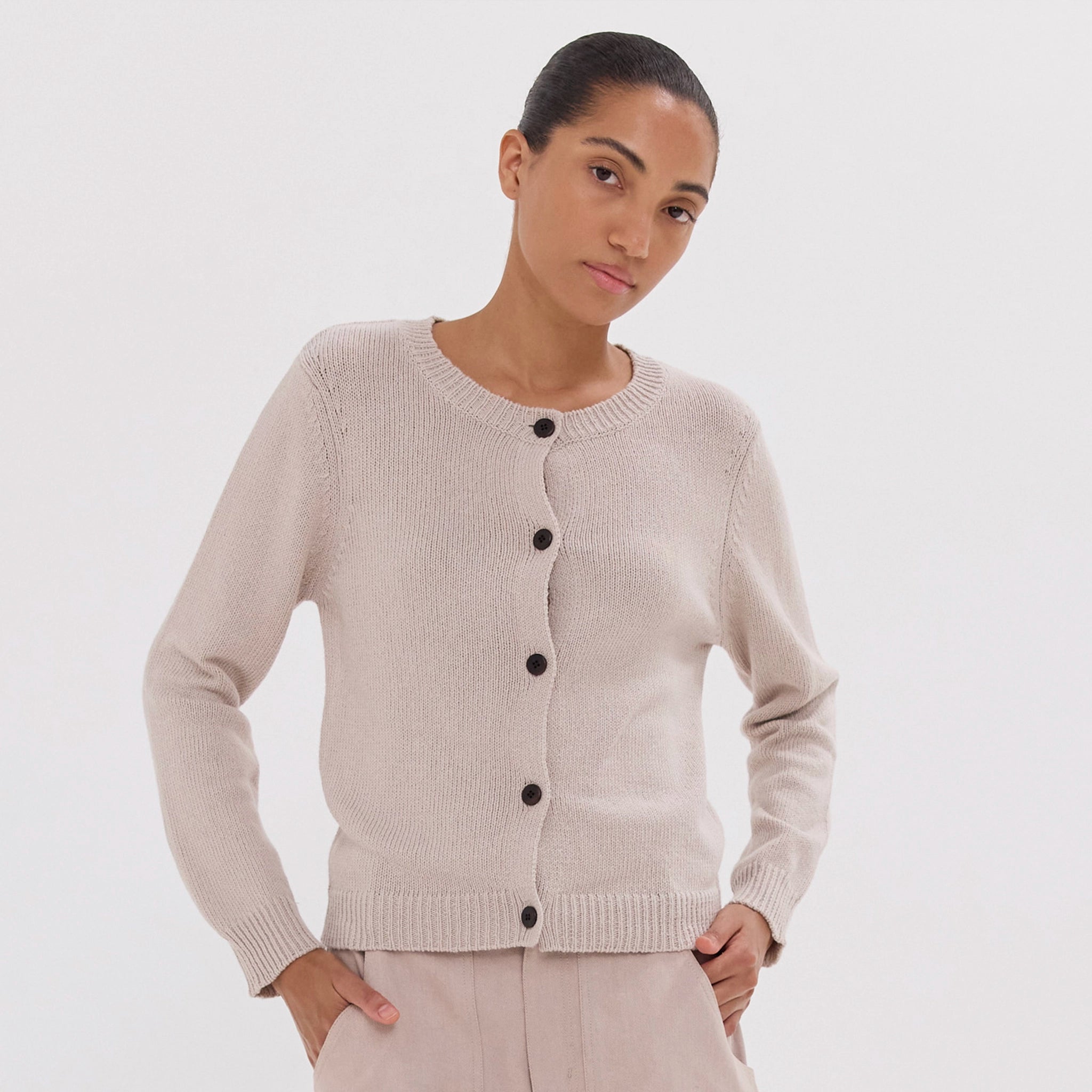 Woman wearing a beige cardigan with black buttons on a white background