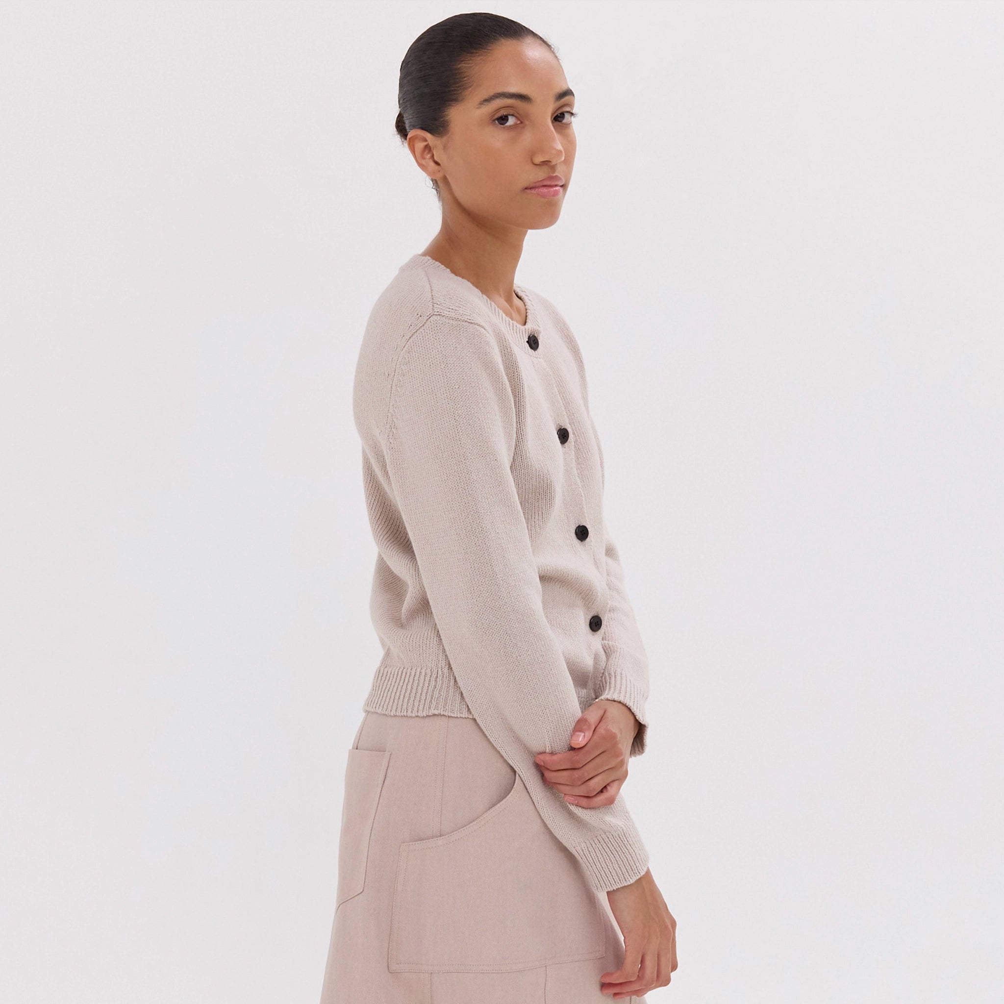 Woman wearing a beige cardigan with black buttons on a white background