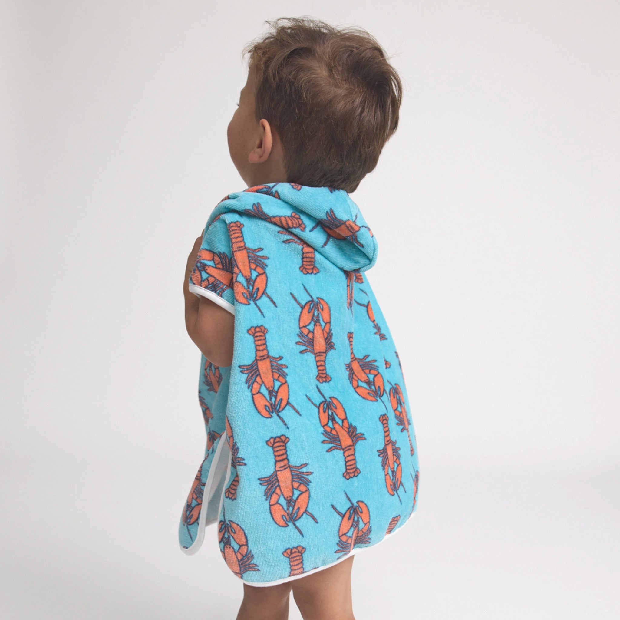 Toddler wearing s hooded poncho with lobster pattern on a light background