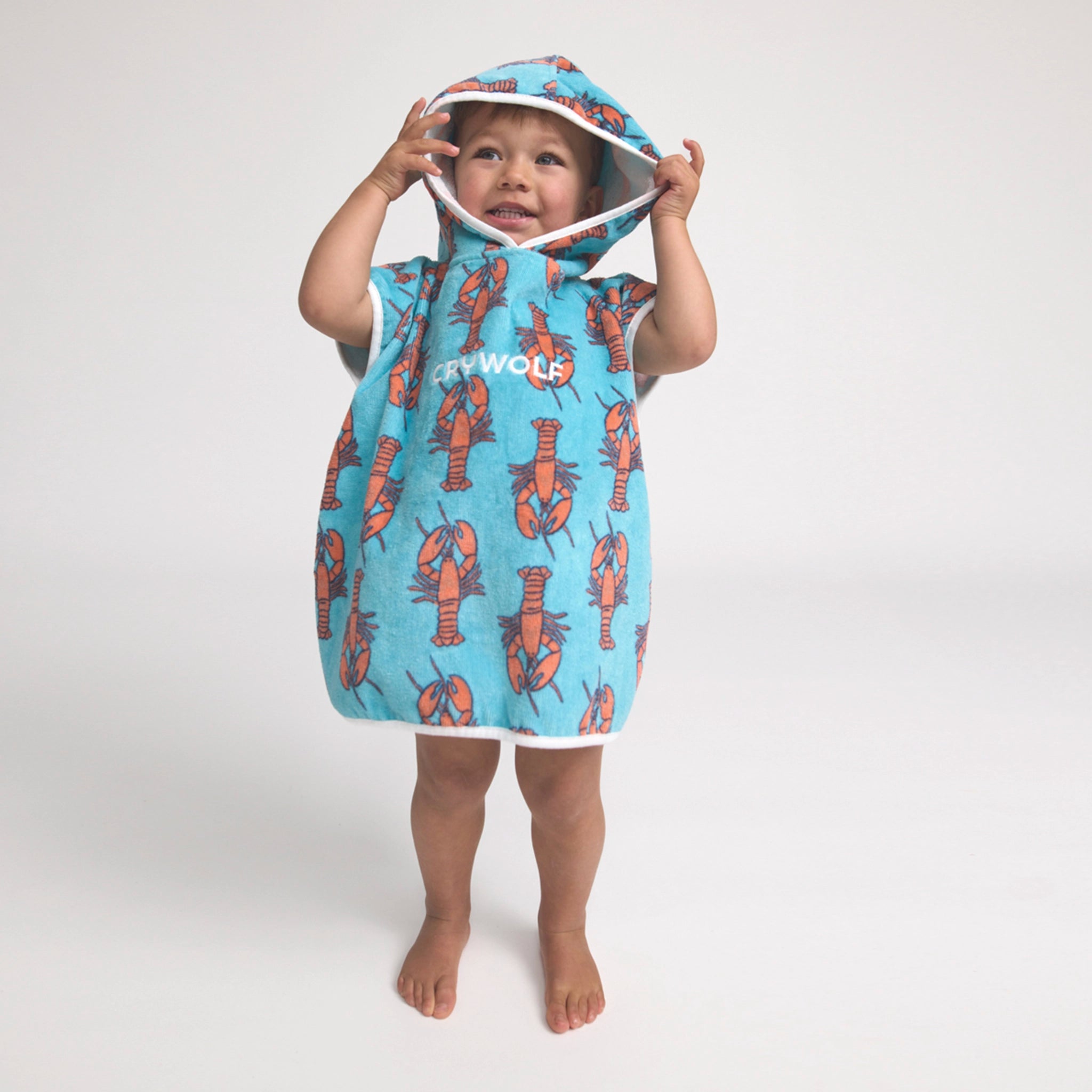 Toddler wearing s hooded poncho with lobster pattern on a light background
