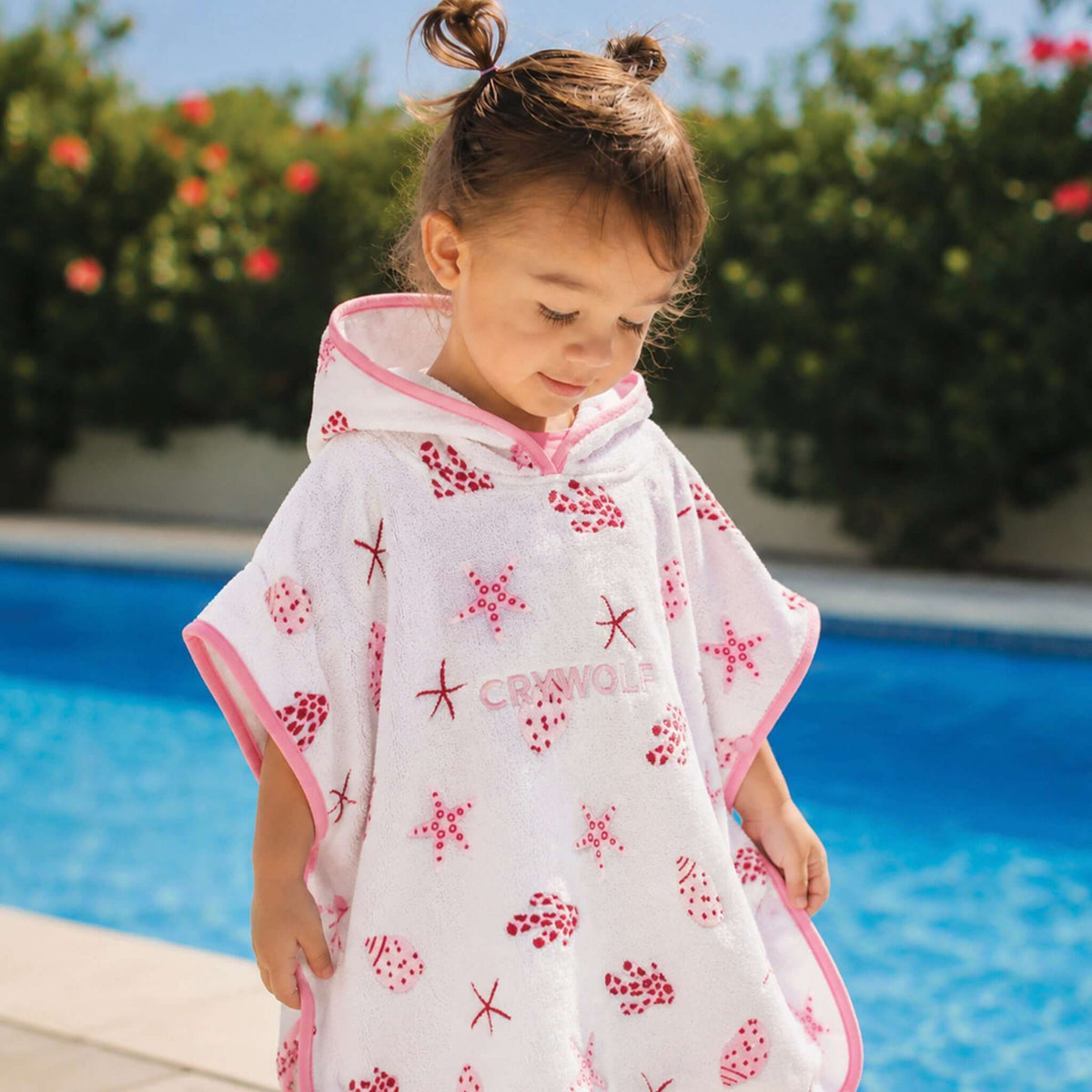 Crywolf Baby Hooded Towel - Little Shell on a child by the pool, featuring vibrant starfish patterns and a cosy hood.