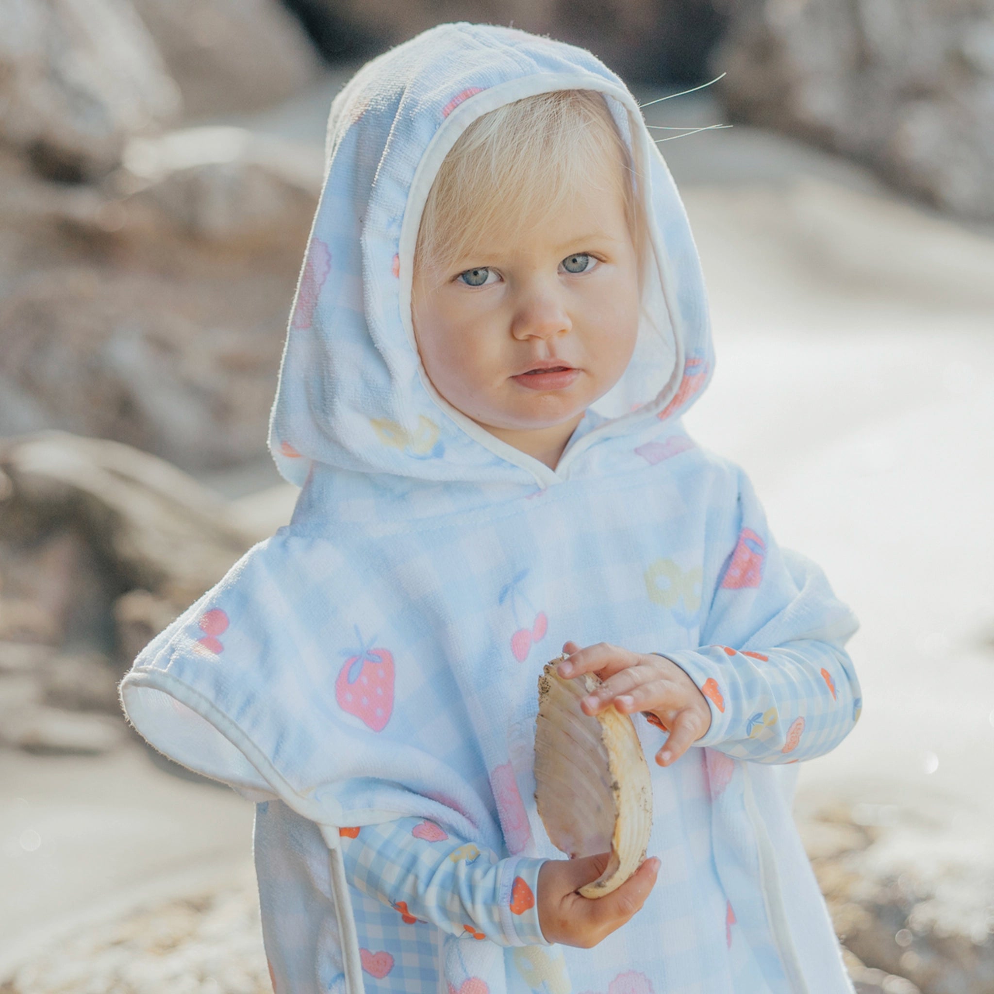 Child wearing a light blue hooded poncho with colorful patterns on a beach.