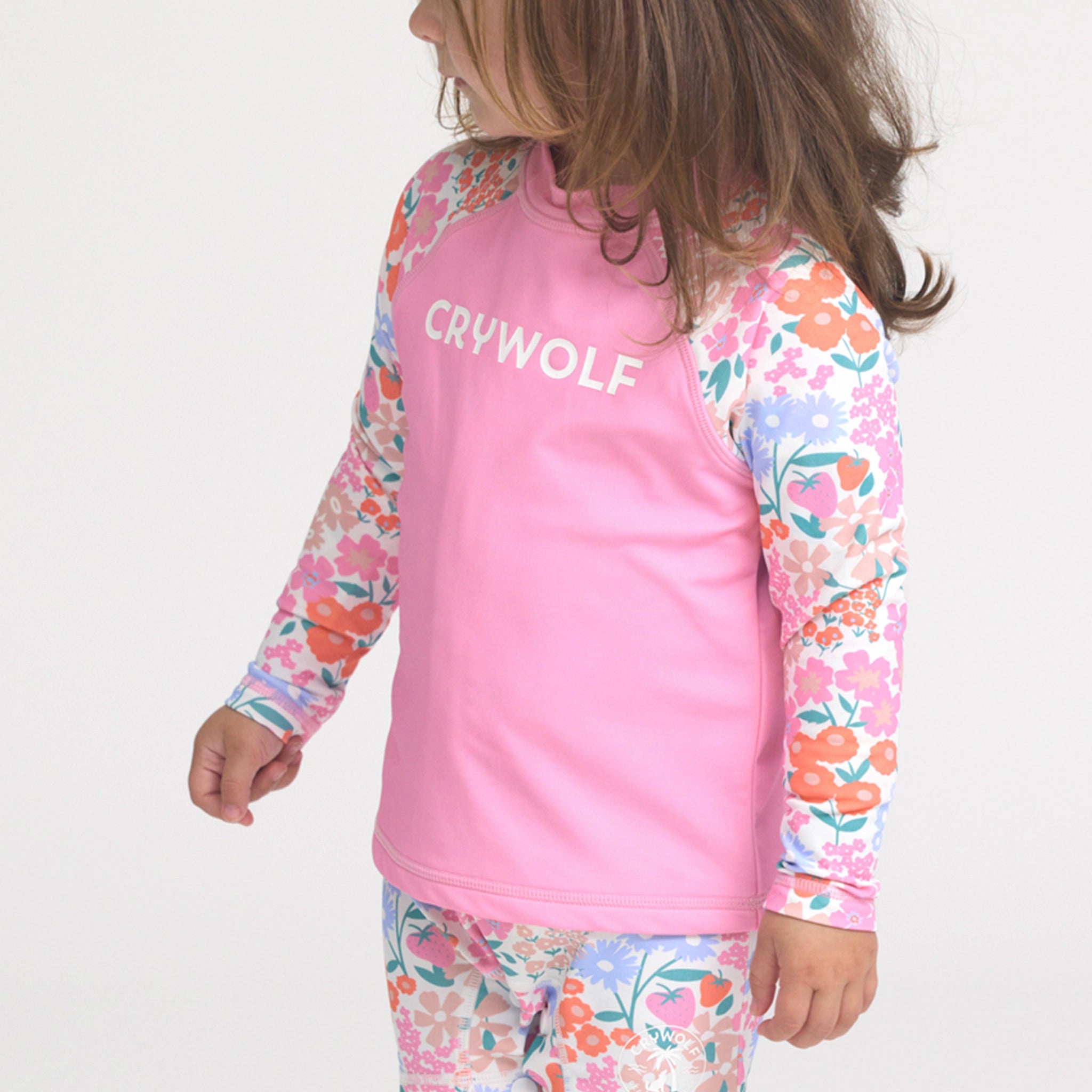 Toddler wearing a pink and floral rash vest on a white background