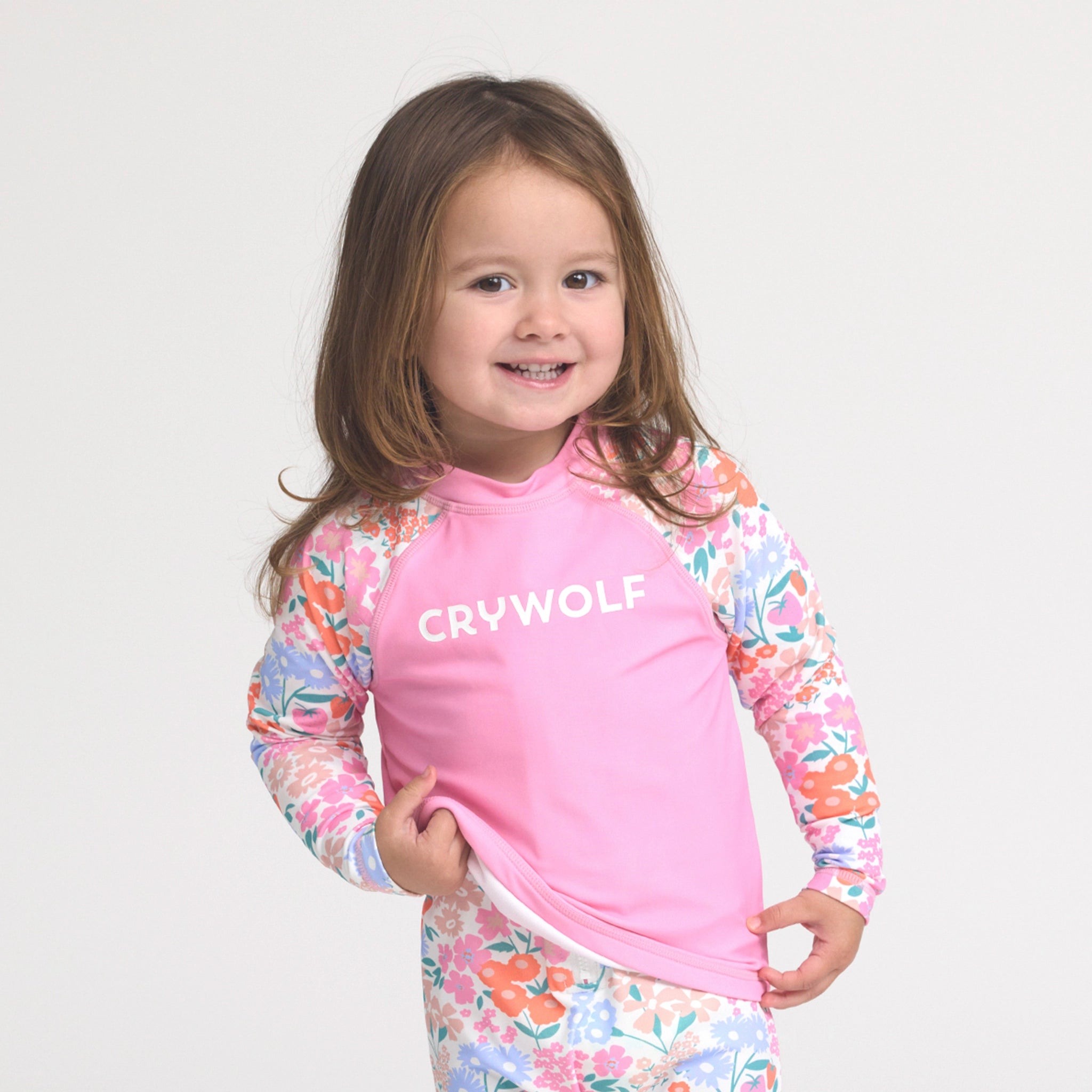 Toddler wearing a pink and floral rash vest on a white background