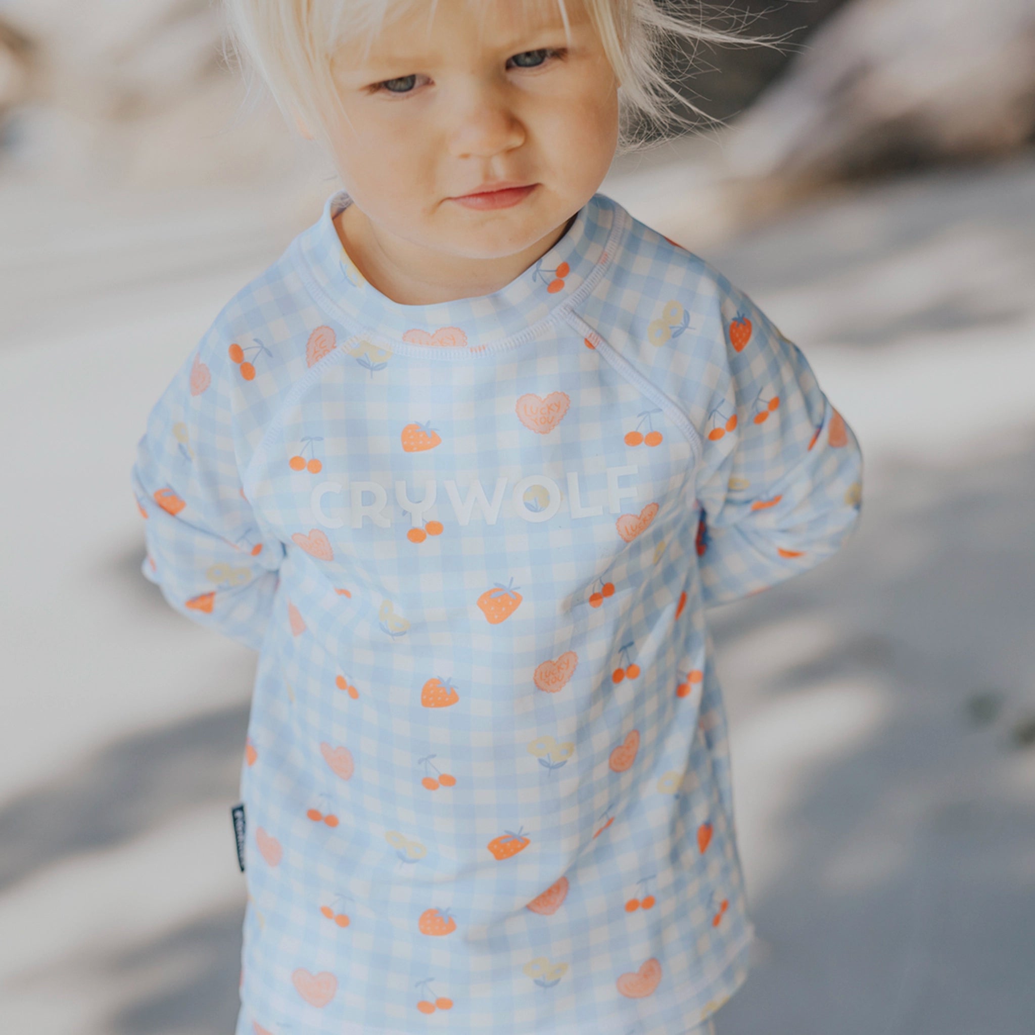 Toddler wearing a blue and pink checkered rash vest at a beach