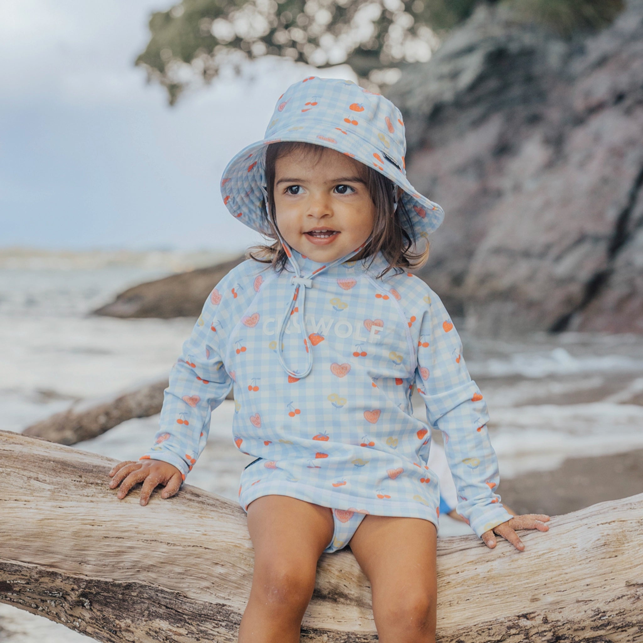 Toddler wearing a blue and pink checkered rash vest at a beach