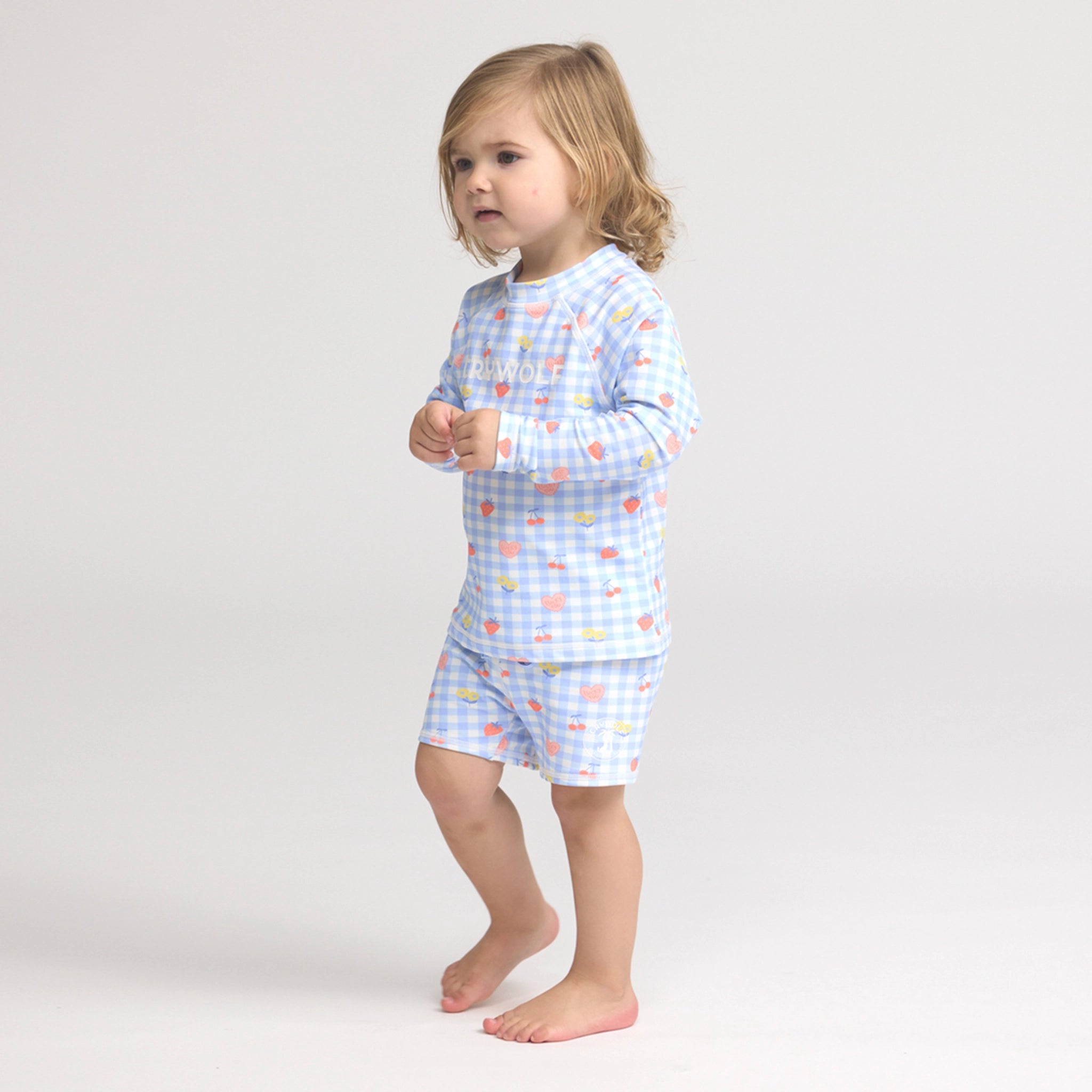 Toddler wearing a blue and pink checkered rash vest on a white background