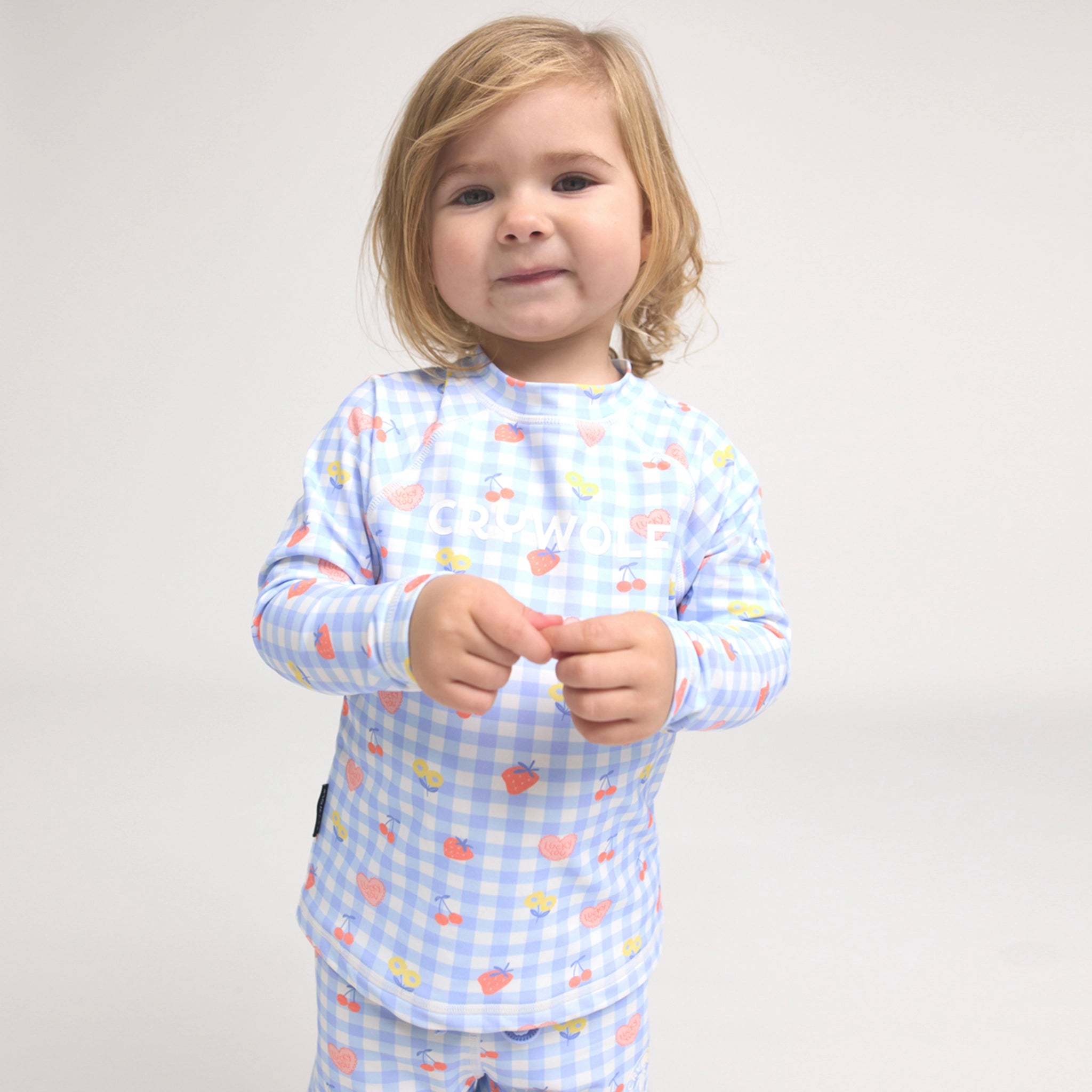 Toddler wearing a blue and pink checkered rash vest on a white background