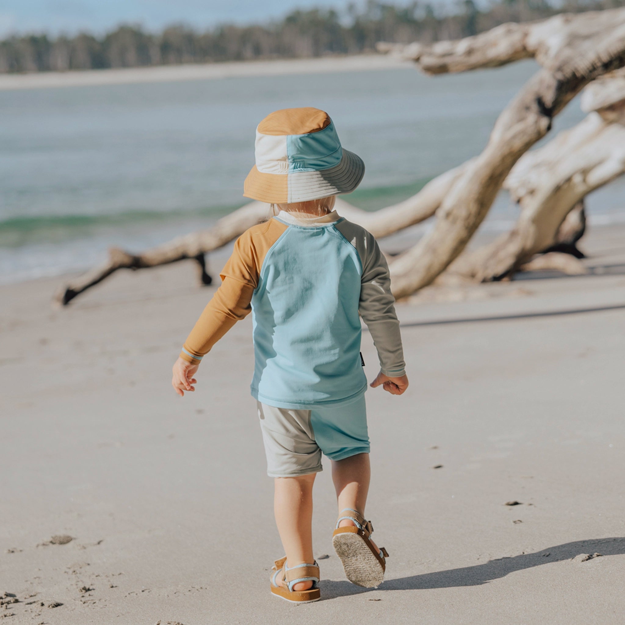 Toddler wearing a brown and blue rash vest at a beach