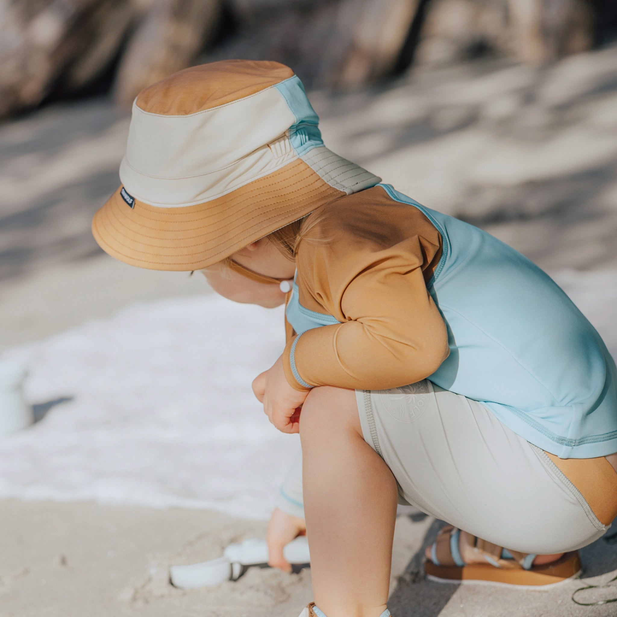 Toddler wearing a brown and blue rash vest at a beach