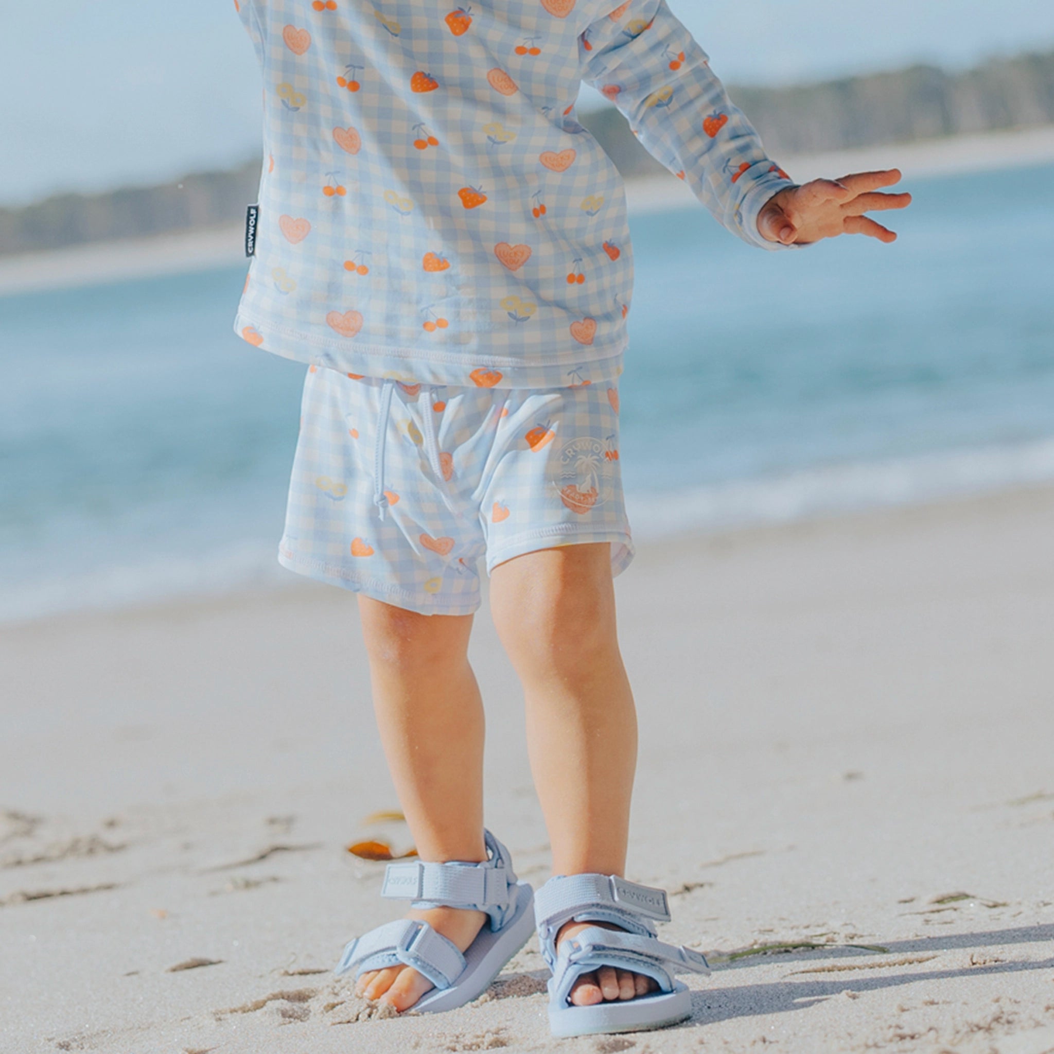 Toddler wearing patterned baby swim shorts on a beach