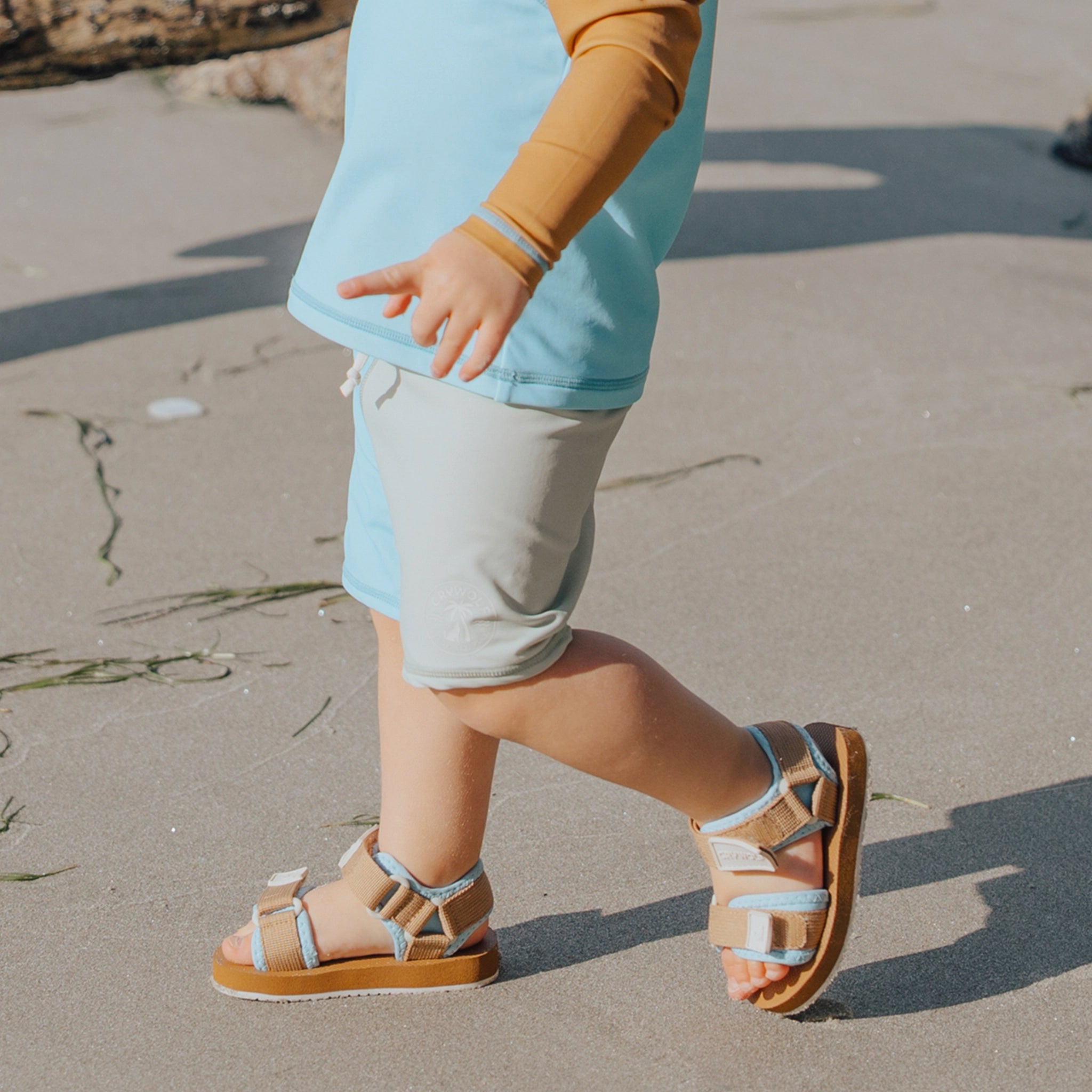 Toddler wearing geometric baby swim shorts on a beach